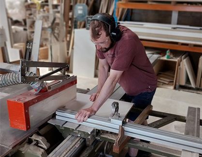 A man wearing headphones is cutting a piece of wood on a machine.