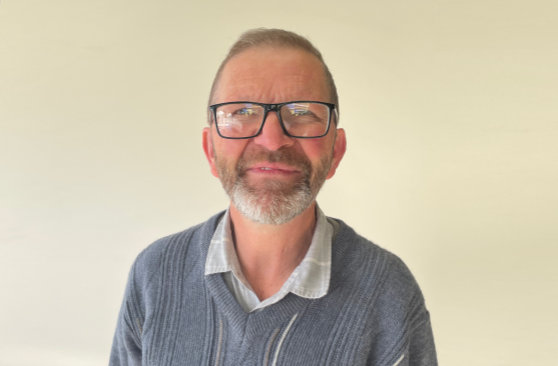 A man with a beard is standing with his arms crossed and smiling.