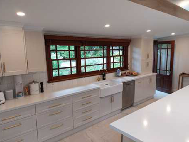 A kitchen with white cabinets , a sink , and a large window.