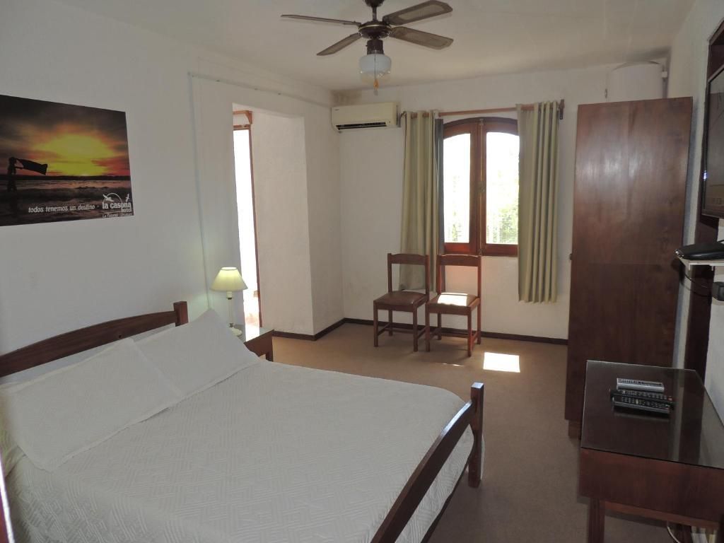 Dormitorio con cama, sillas, armario, ventana y lámina con una puesta de sol.