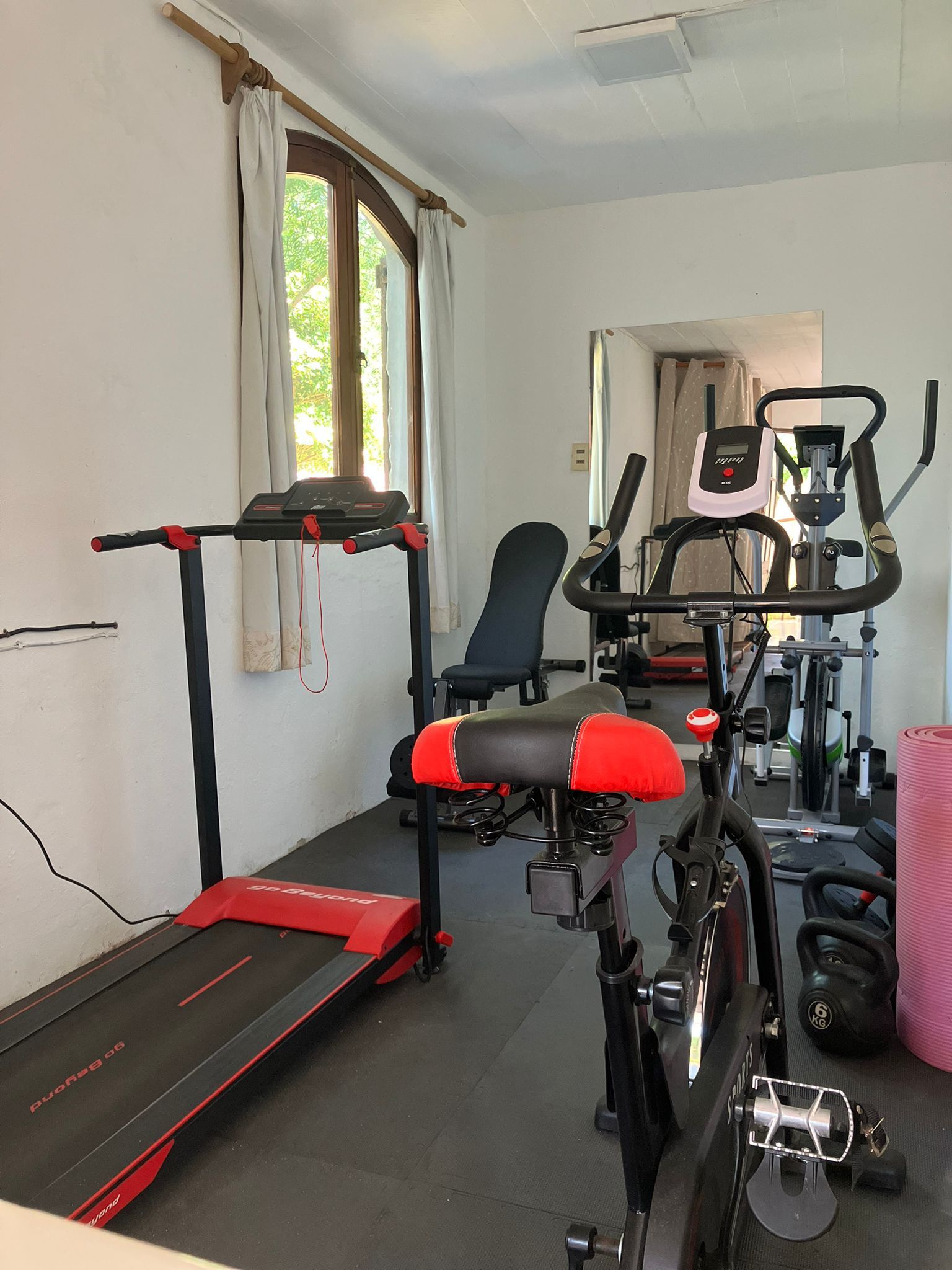 Gimnasio en casa con cinta de correr, bicicleta estática, banco de pesas y equipo de ejercicio.
