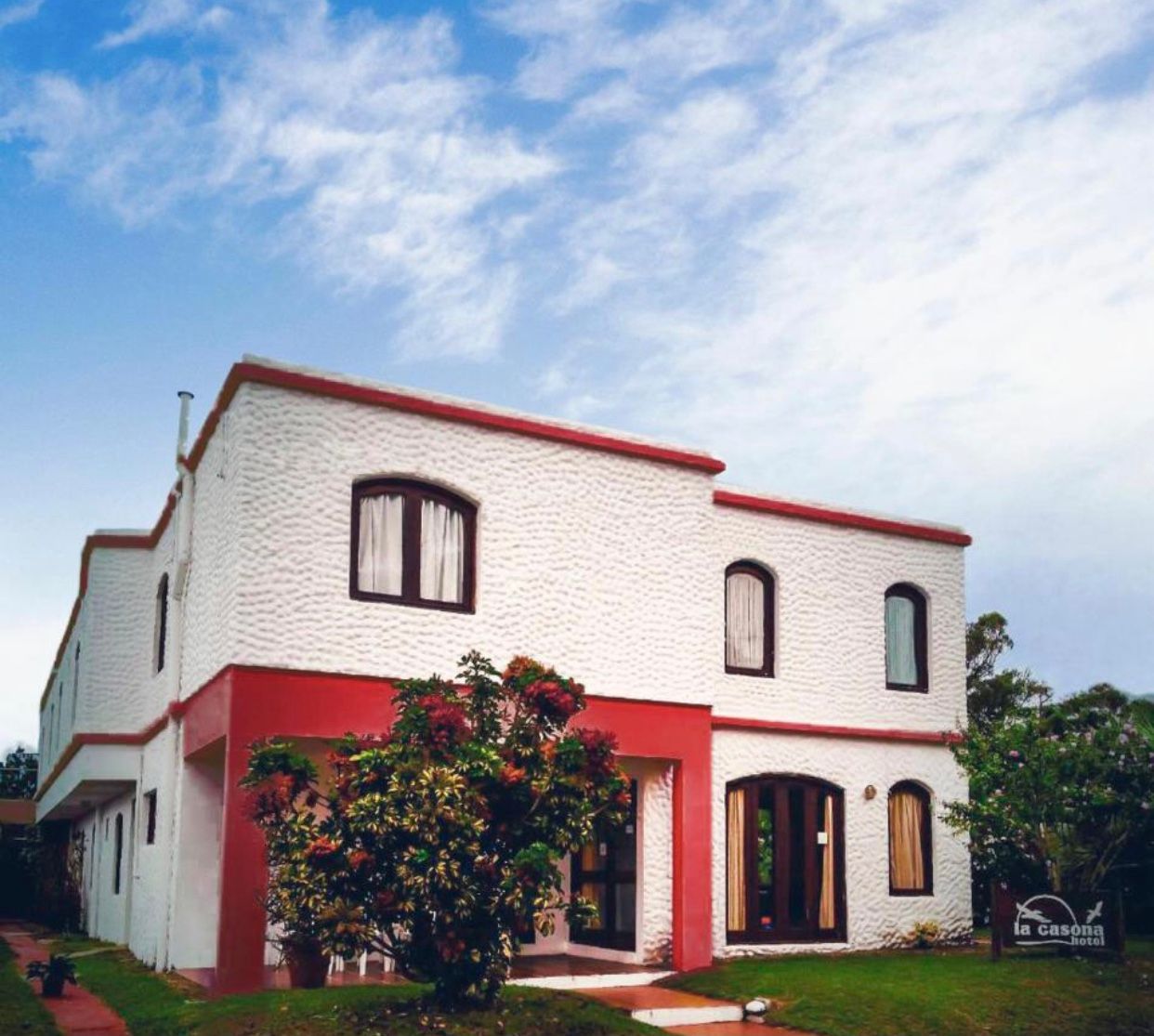 Edificio blanco de dos plantas con detalles rojos, ventanas arqueadas y cielo azul.