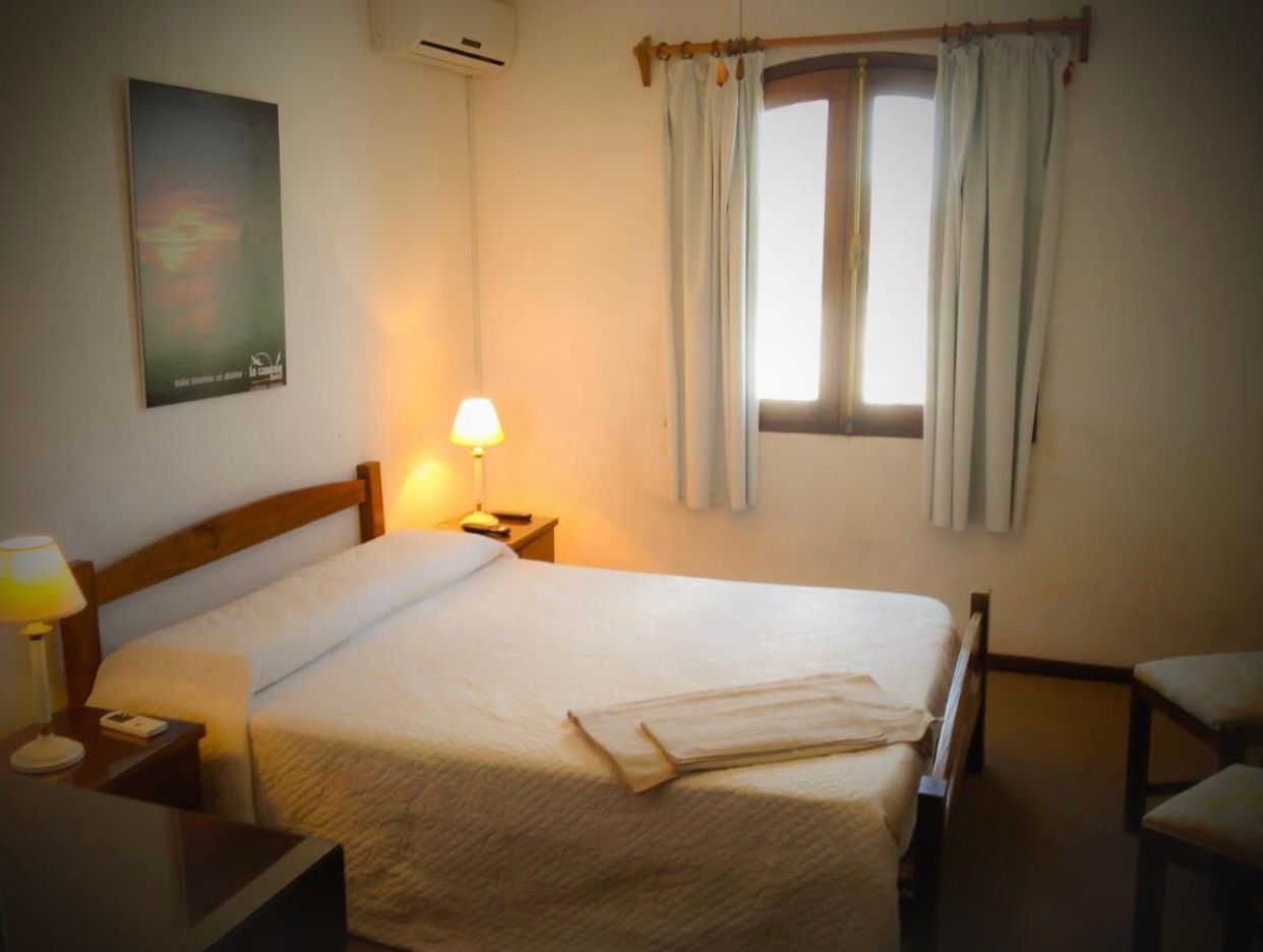 Dormitorio con cama doble, mesitas de noche, lámpara, ventana con cortinas y cuadro en la pared.