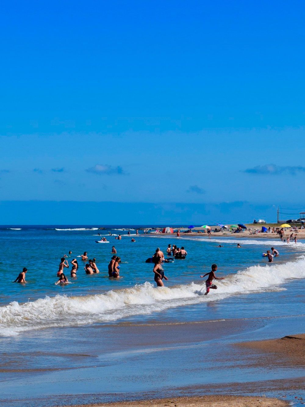 Personas nadando en las olas del océano en una playa en un día soleado.