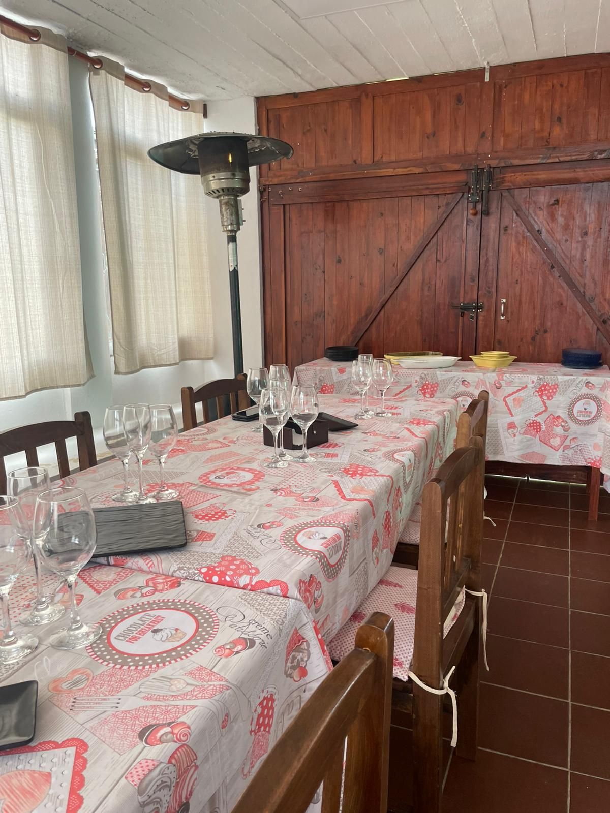 Mesa de comedor larga para invitados, con cristalería, mantelería estampada y calentador de exterior.