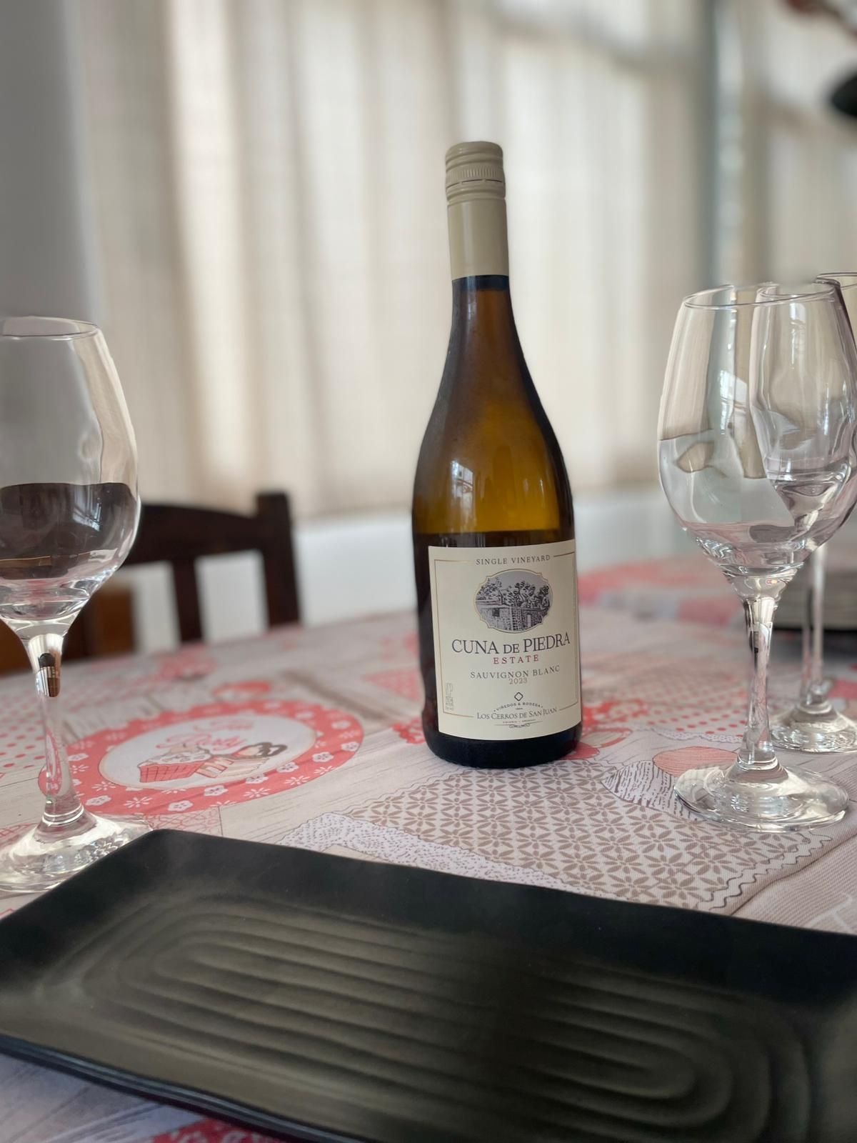 Una botella de vino y copas sobre una mesa. El mantel es blanco y rojo.