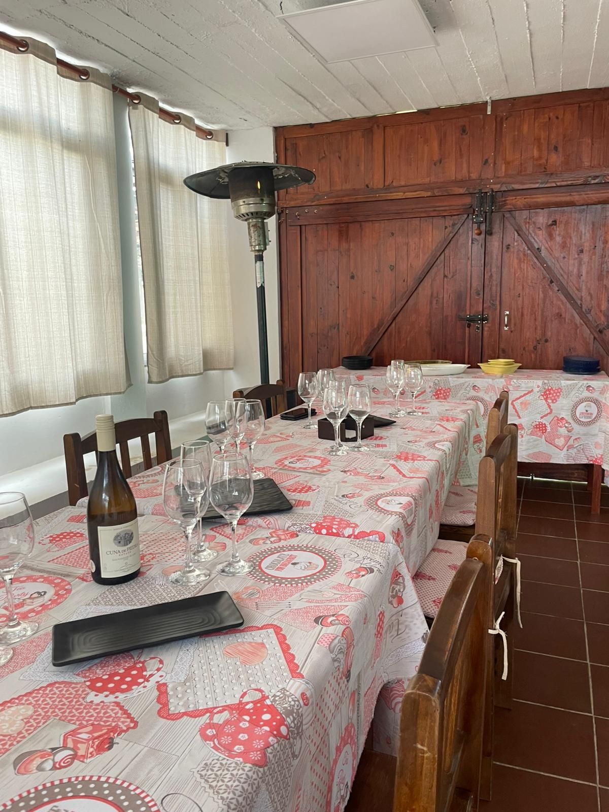 Mesa de comedor con copas de vino, botella y platos, con mantel floral. Decoración interior.