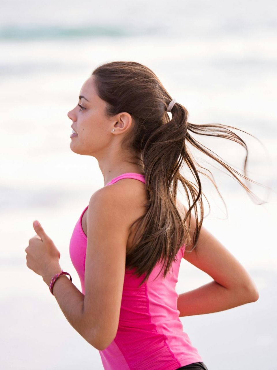 Mujer con top deportivo rosa corriendo cerca del agua.