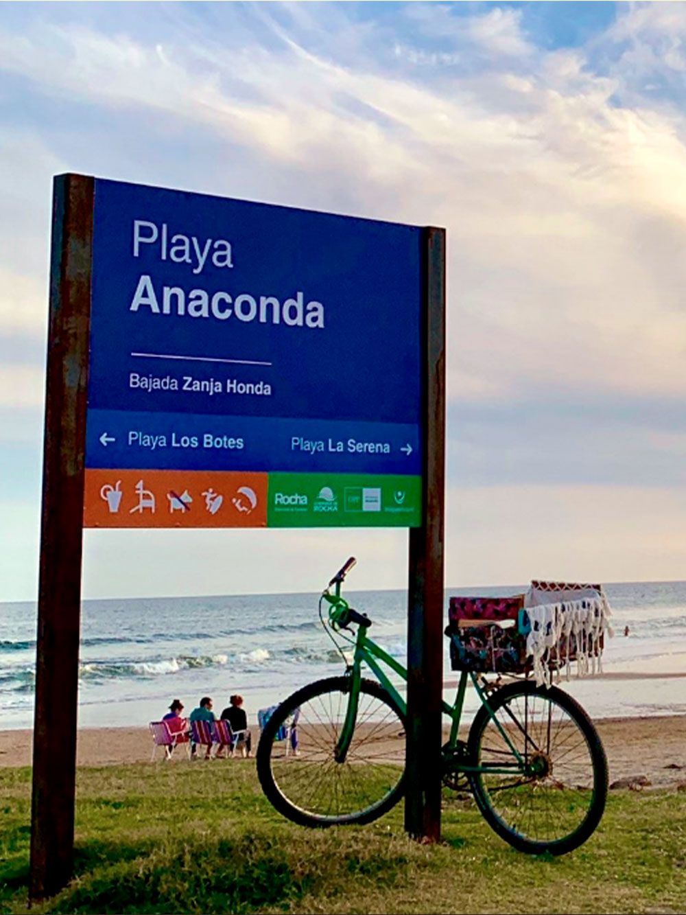Letrero para la playa Anaconda, con una bicicleta verde al frente, océano y cielo de fondo.