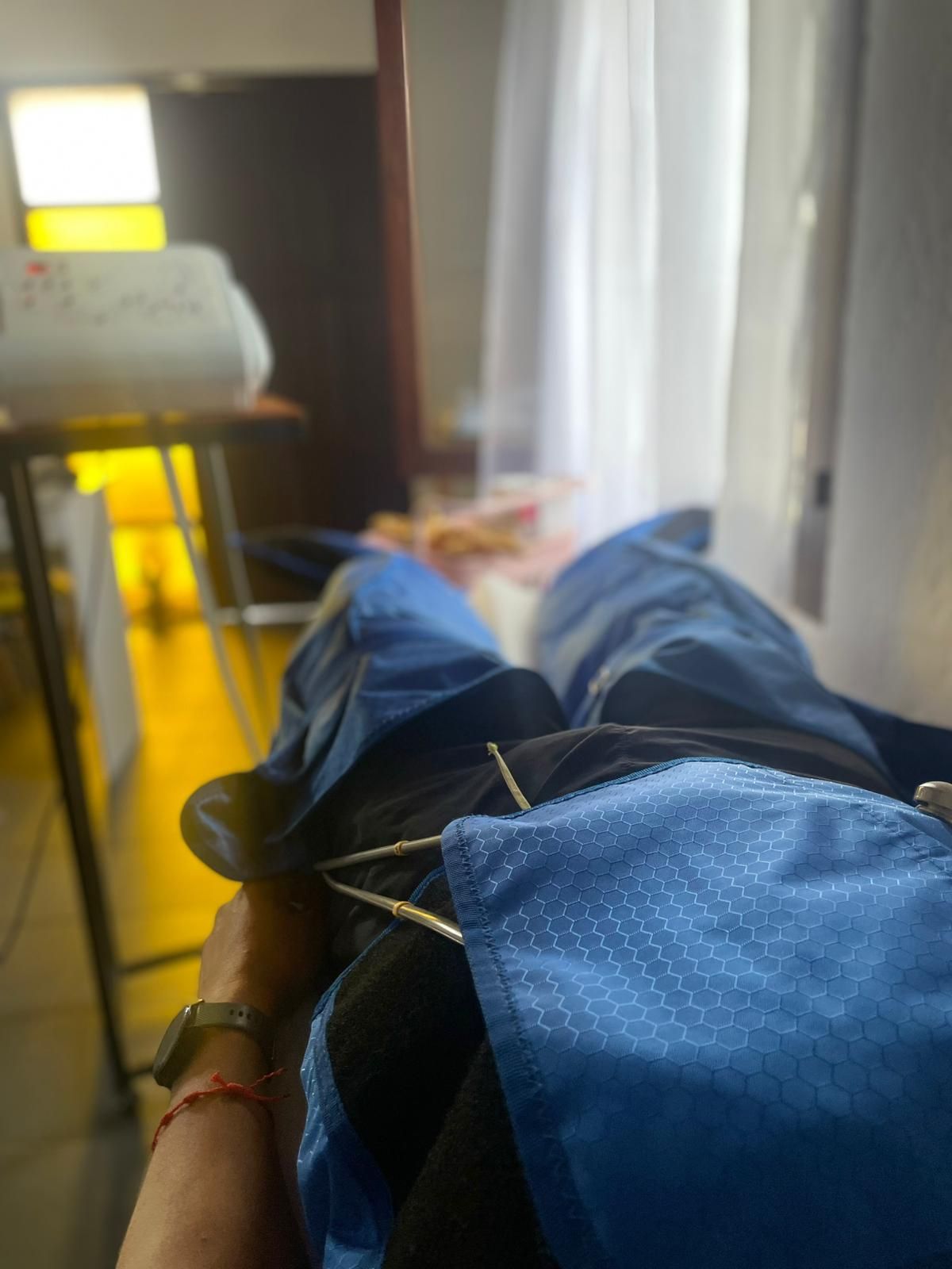 Persona reclinada, con pantalones azules y una manta azul. El entorno aparece en un interior, cerca de una ventana