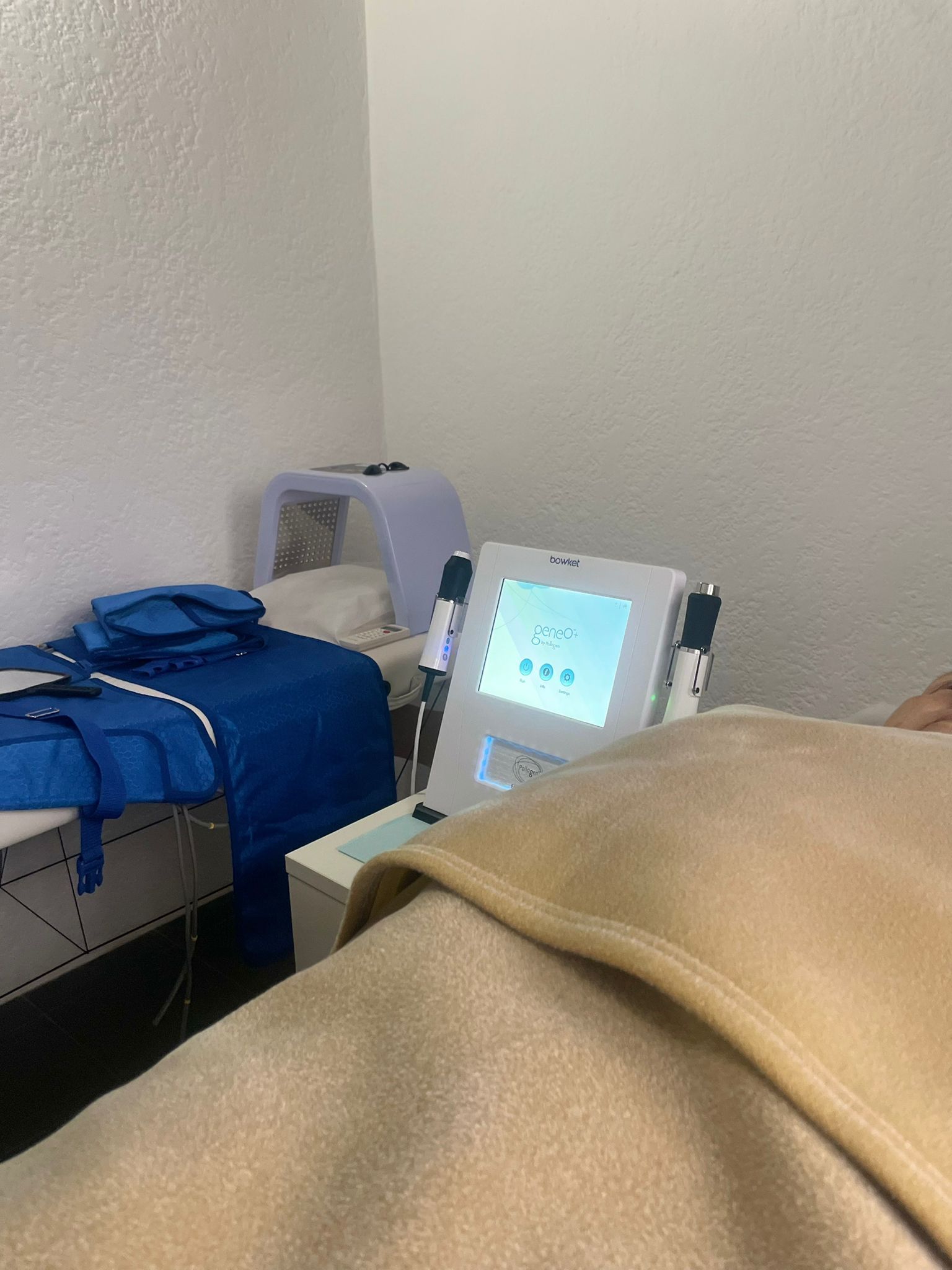 Una sala médica con una persona cubierta por una manta, una máquina y una cama con mantas azules.