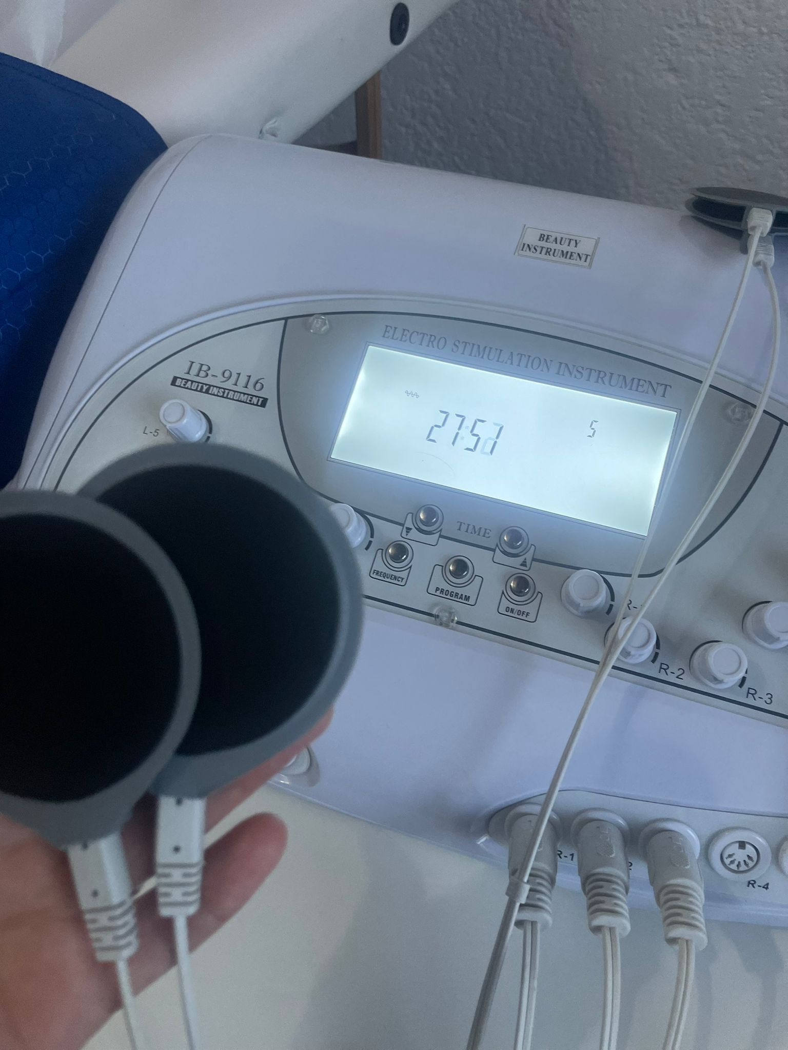 Mano sosteniendo dos electrodos redondos delante de una máquina de electroterapia blanca.