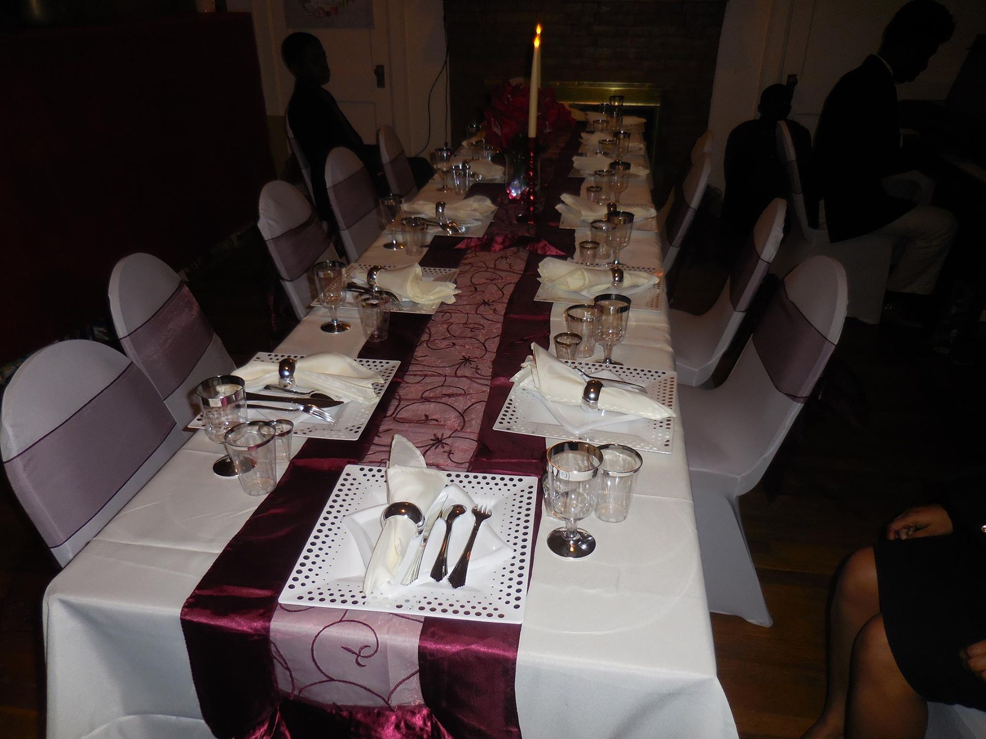 A long dining table set for an event with white tablecloths, deep purple runners, and matching chair covers.