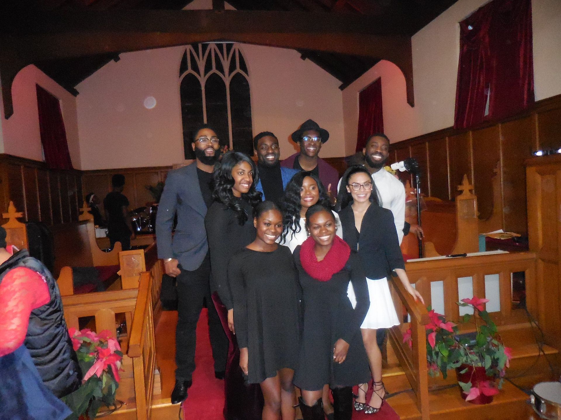 A group of people posing for a photo in a church sanctuary, standing on a red carpet in front of wooden pews and decor.
