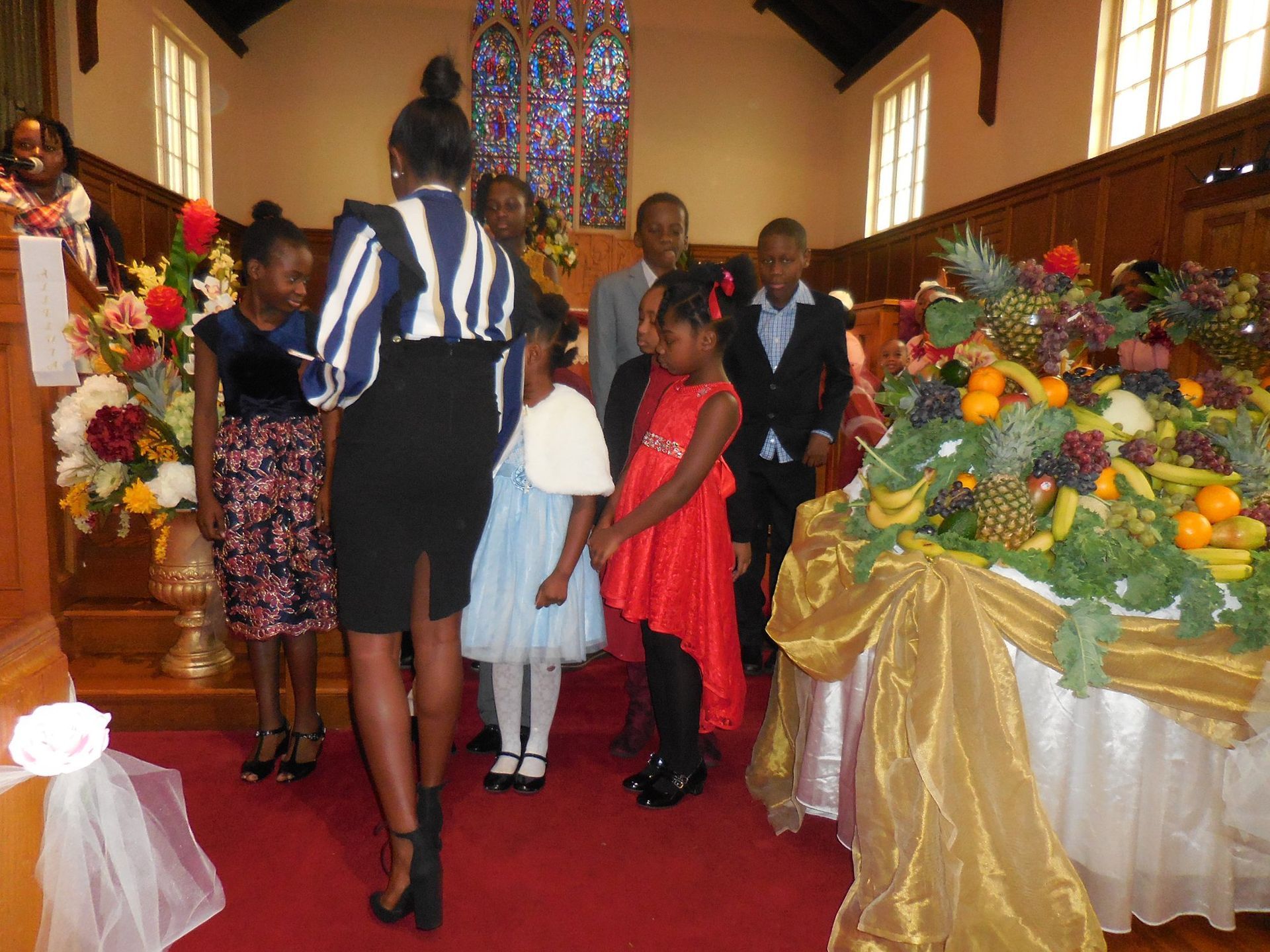 A group of people standing in a church with a large display of fruit and flowers on a table in the foreground.