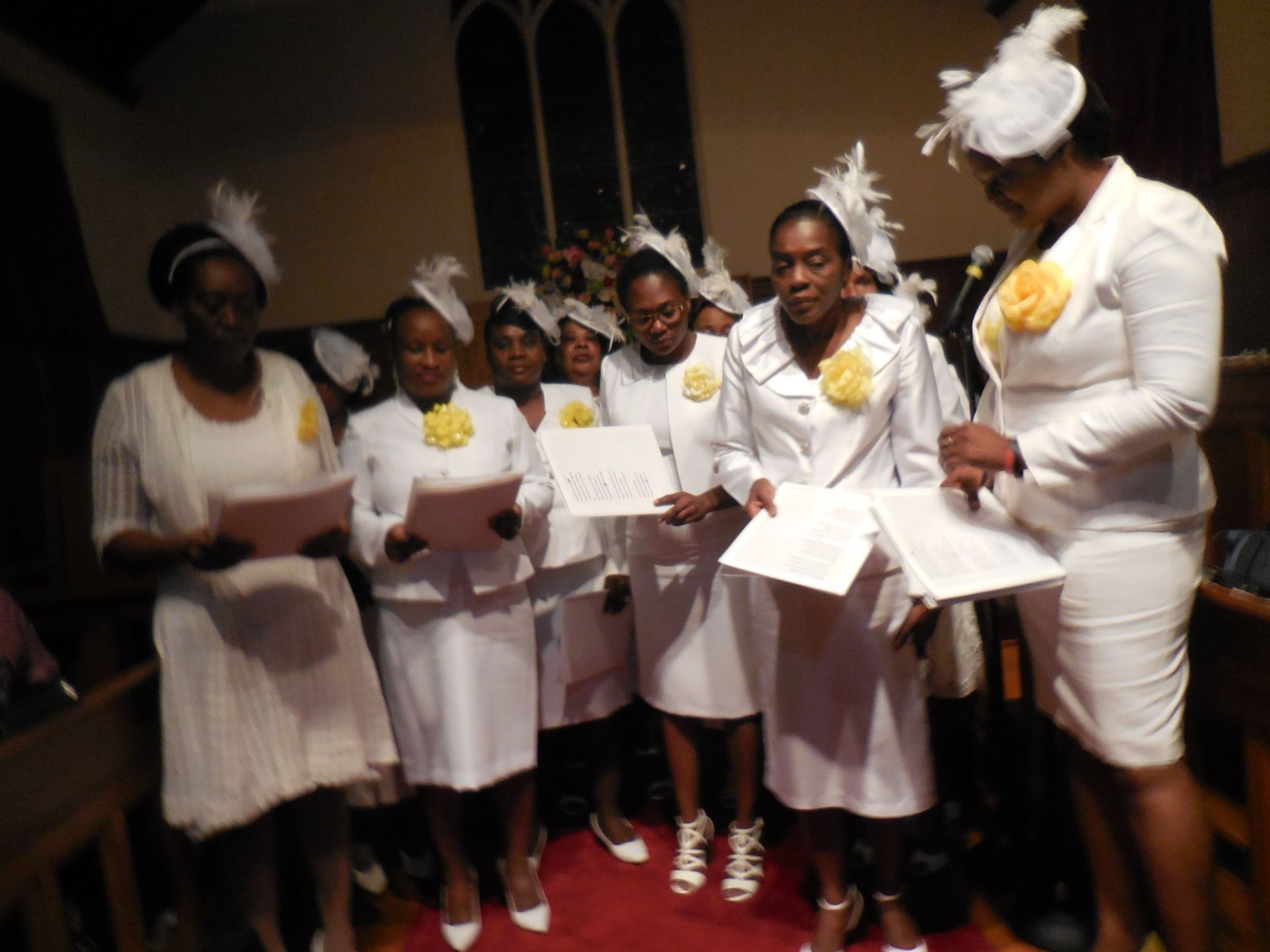 A group of people dressed in white outfits and hats, holding papers and singing in a church setting.
