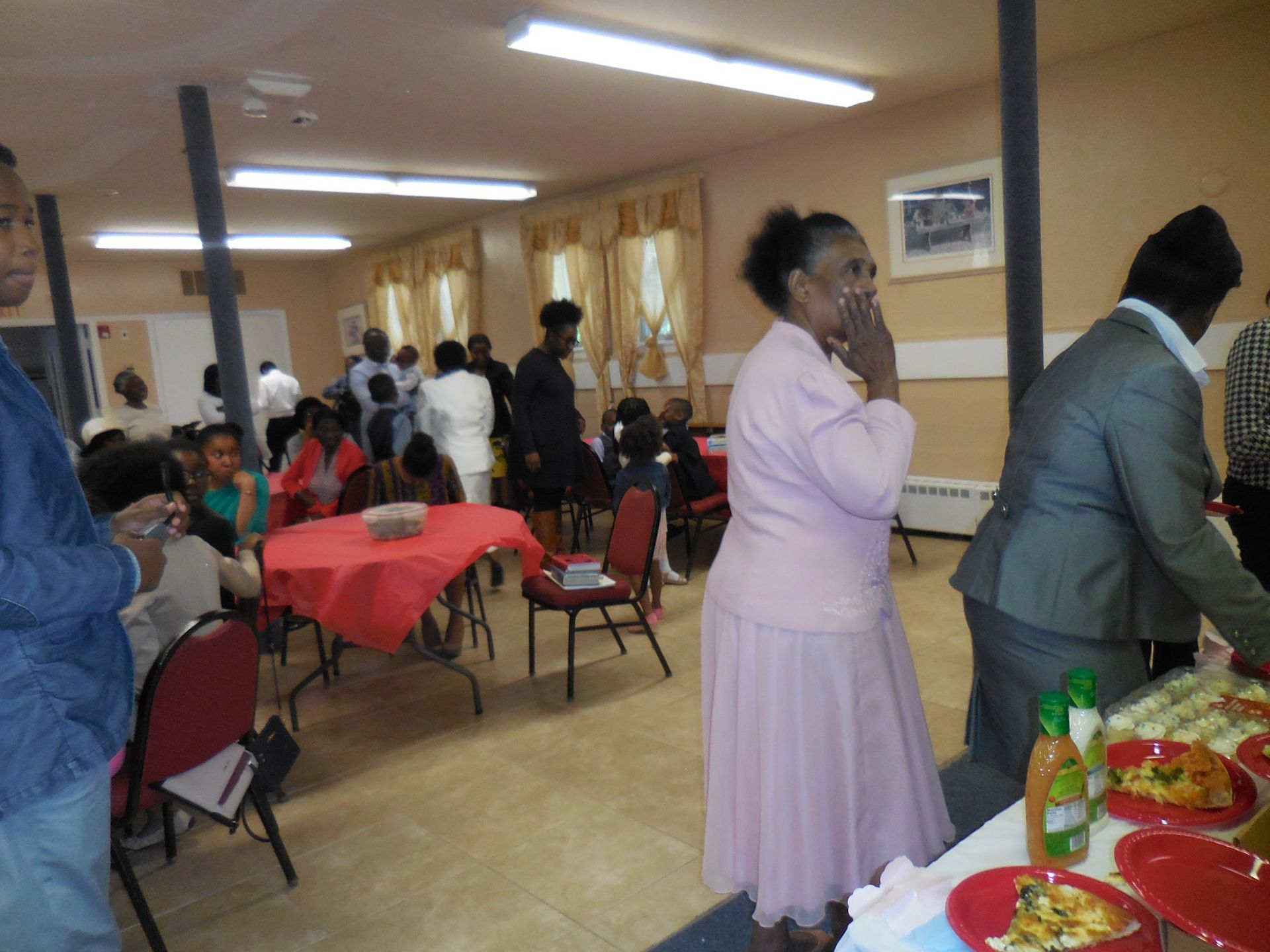 People gather in a bright community room for a meal, with food arranged on tables in the foreground.