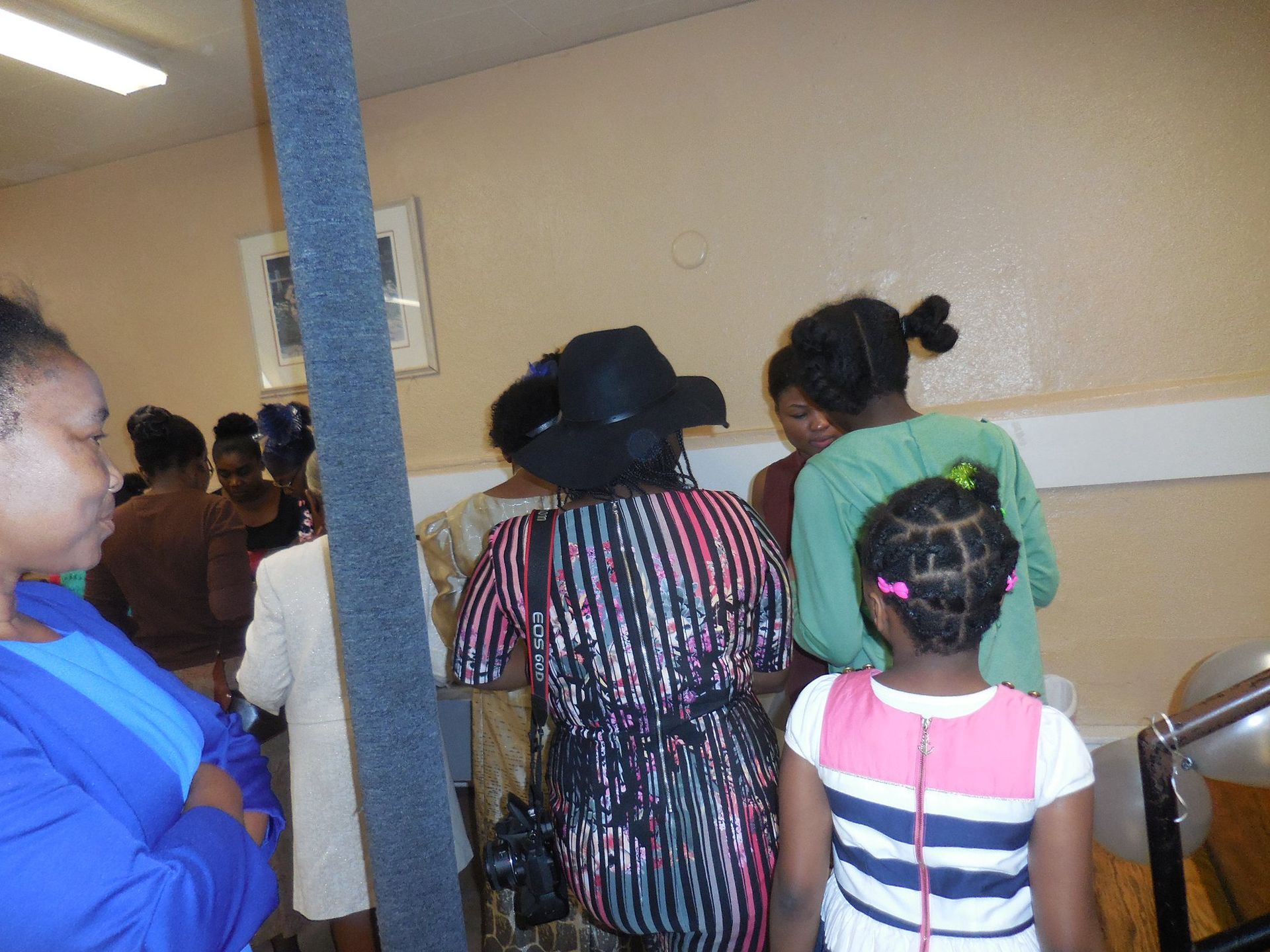 A group of people wearing varied attire gathers indoors, standing together in a room.