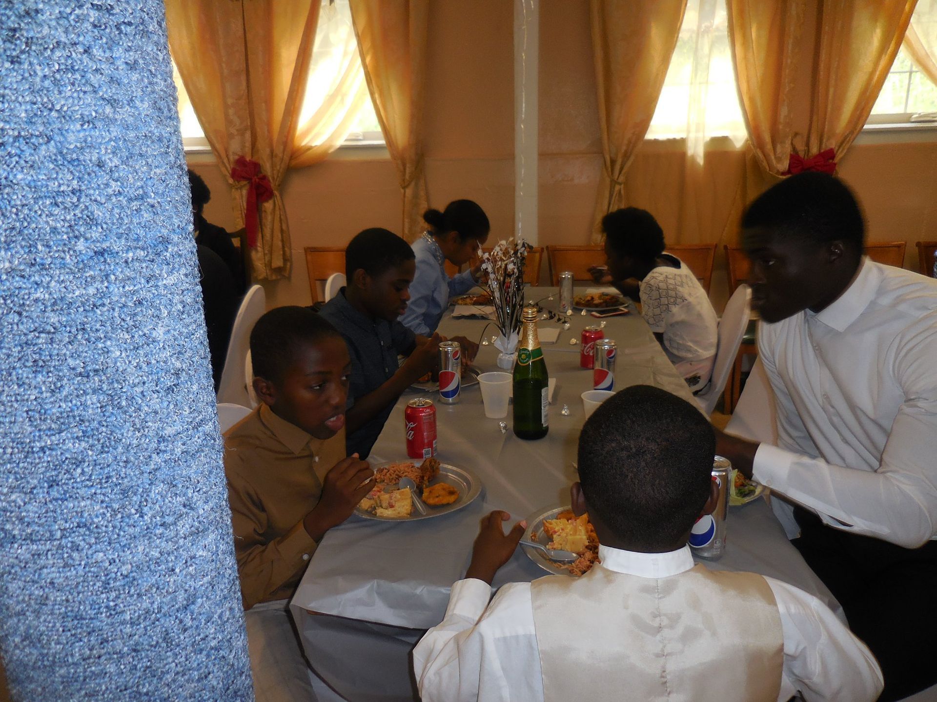 People eat at a table in a room with light curtains and blue pillar decor.