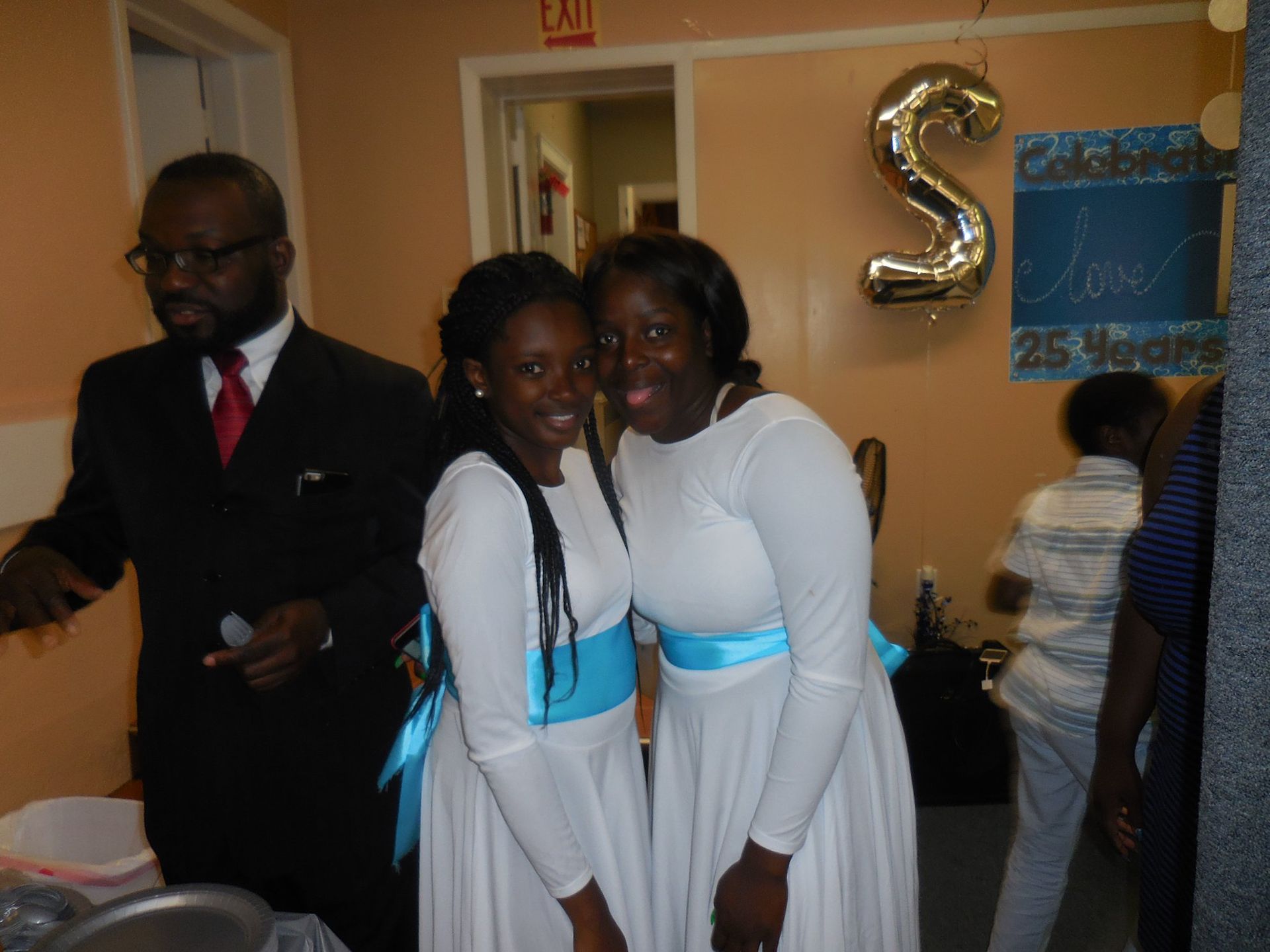 A man in a suit and two people in matching white dresses with blue sashes pose at an event with 