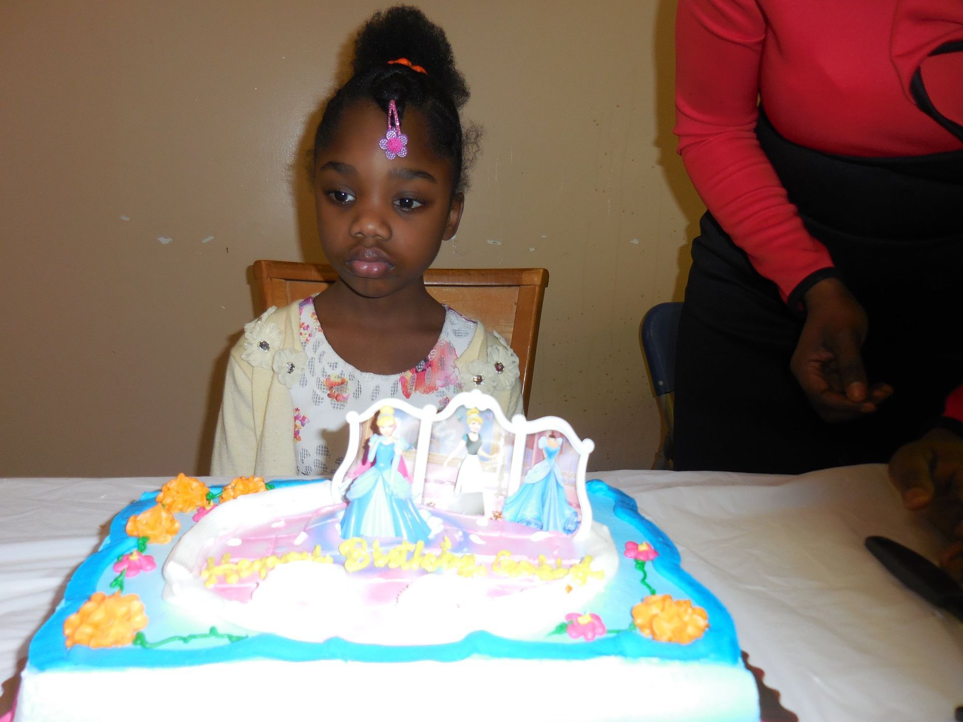 A young child sits behind a rectangular, light blue and white birthday cake featuring Cinderella decorations.