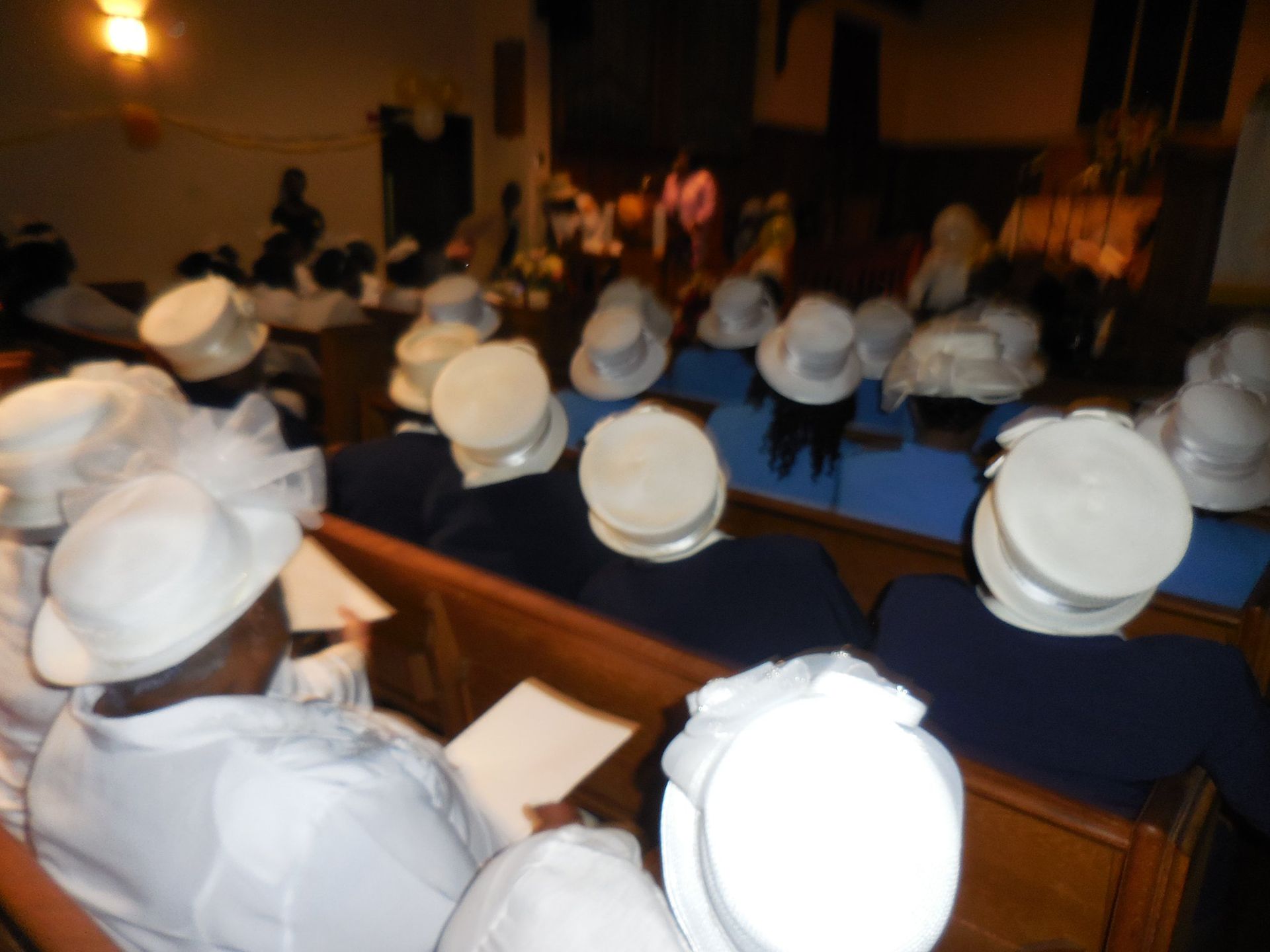 A group of people wearing white hats and matching outfits seated in church pews during a service.