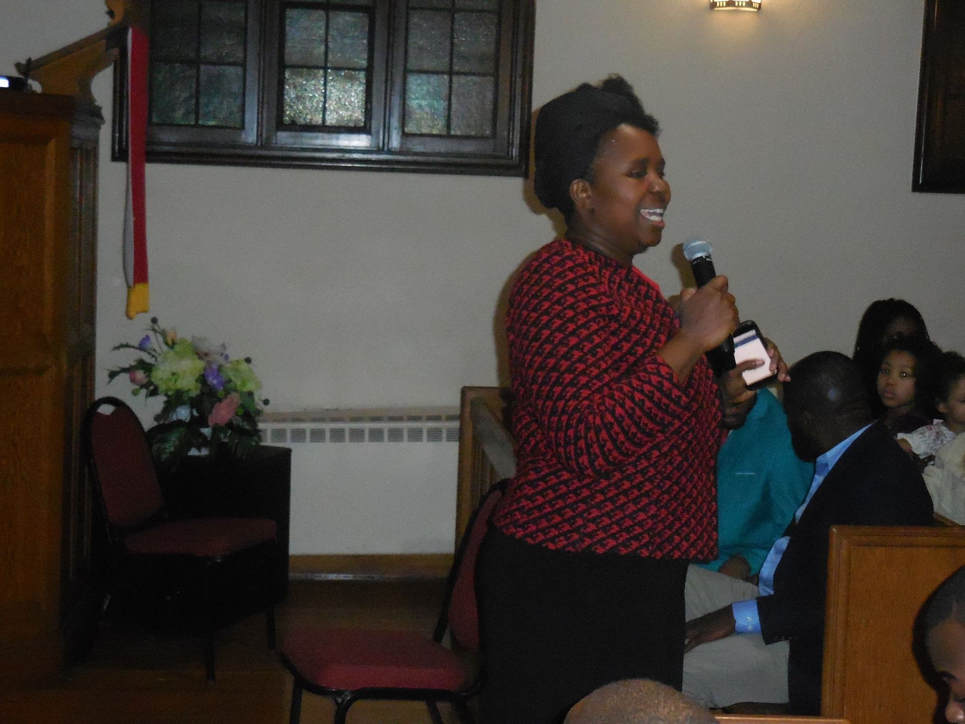 A person speaking into a microphone while standing in front of an audience in a church setting.