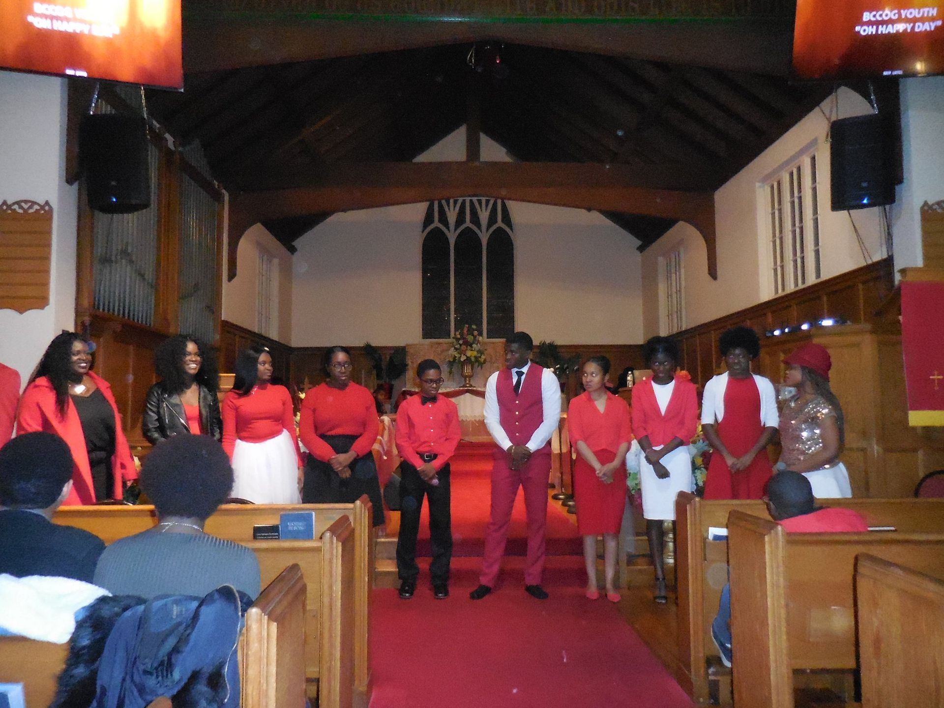 A group of people wearing red and black attire stand in a church aisle during an event.