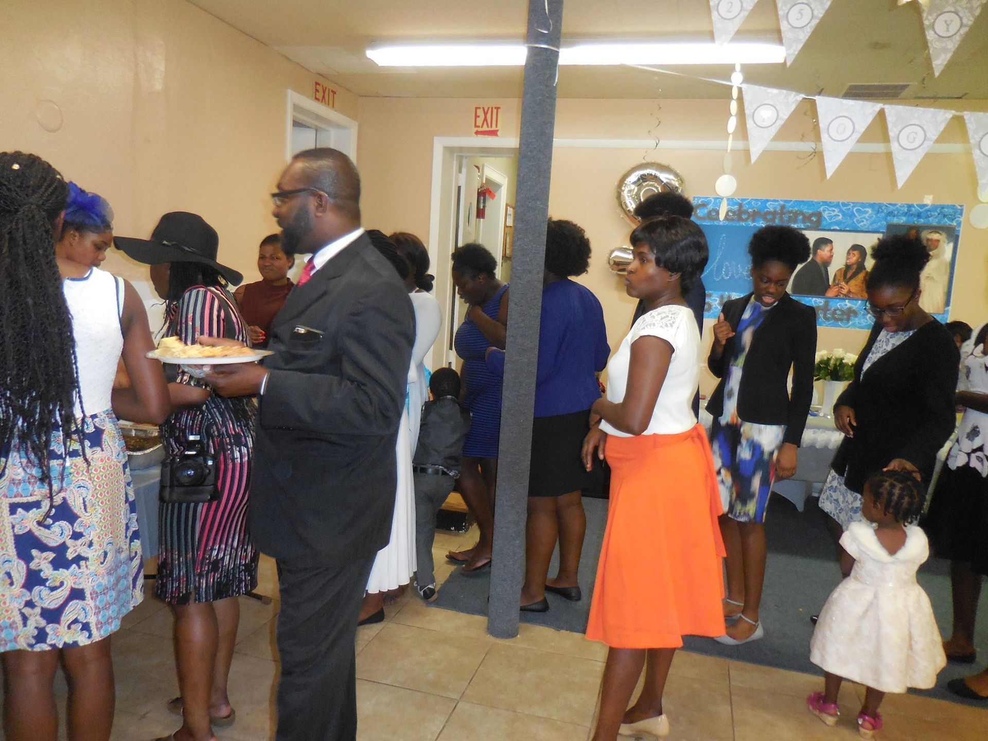 A group of people standing in a room during a gathering, with some standing at a buffet table.