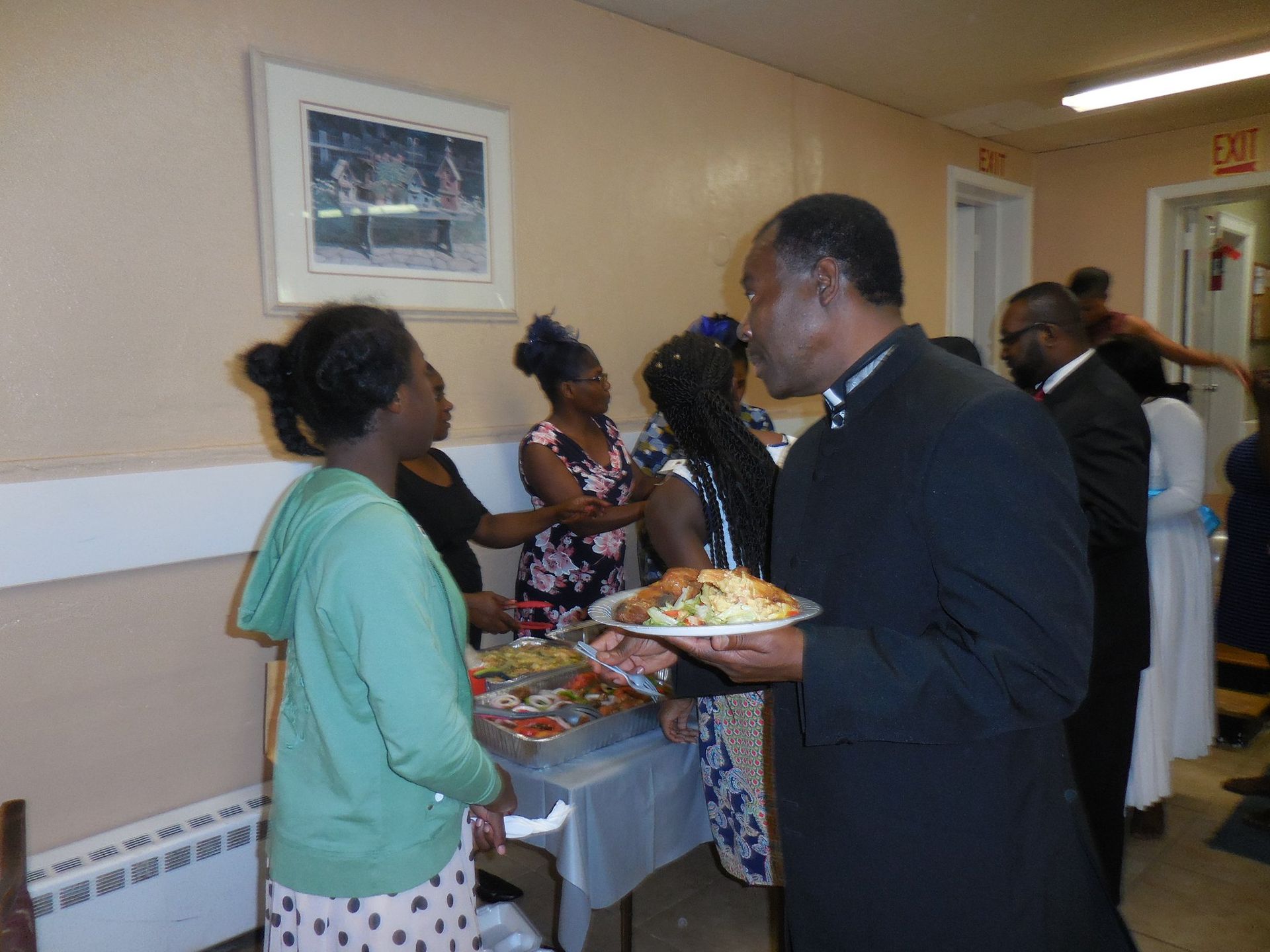 People stand near a buffet table with food at an indoor gathering.