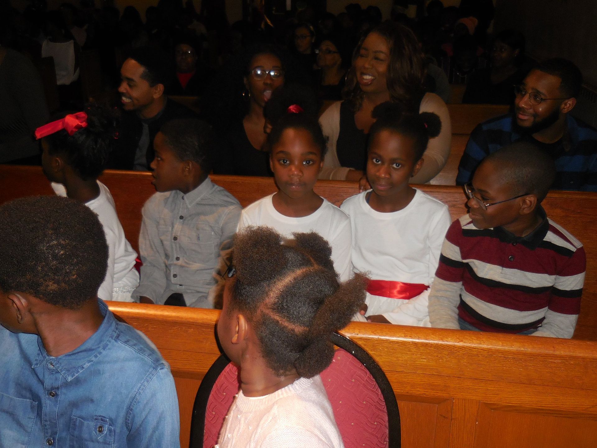 A group of people sitting in church pews during a service, some looking towards the front and others towards the camera.