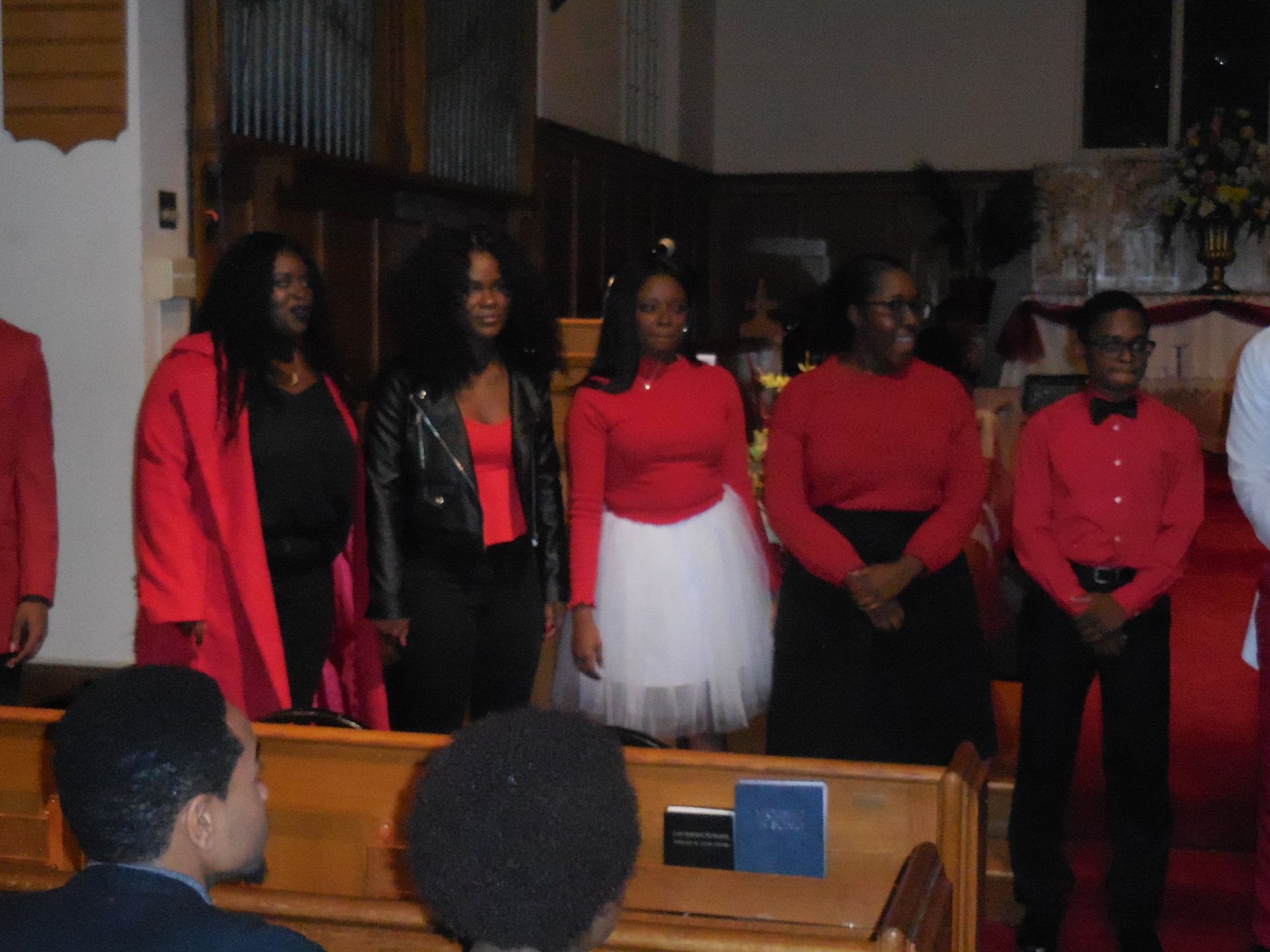 A group stands on a church stage wearing red and black, facing forward.