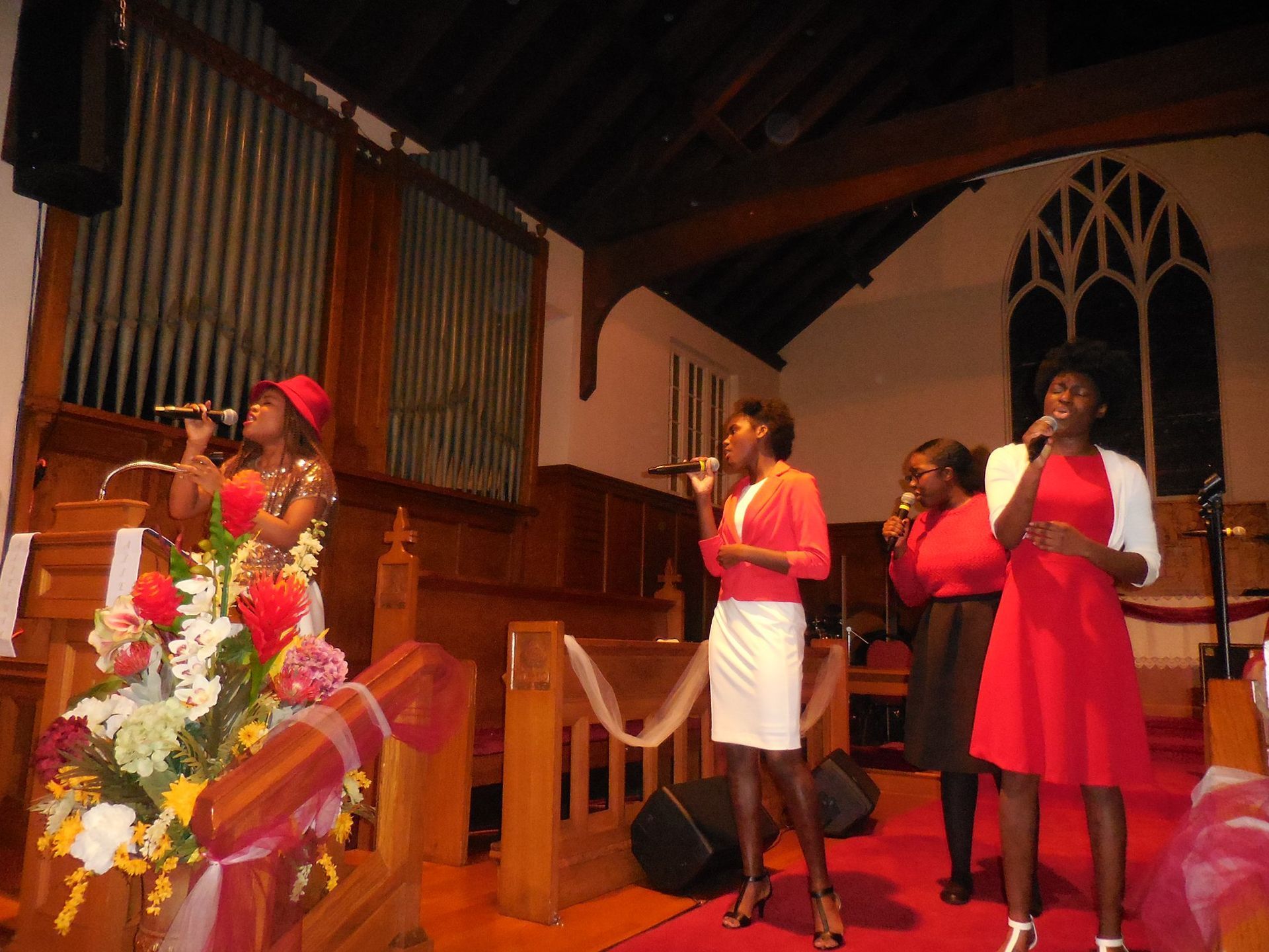 Four people in formal attire singing into microphones on a stage in a church.