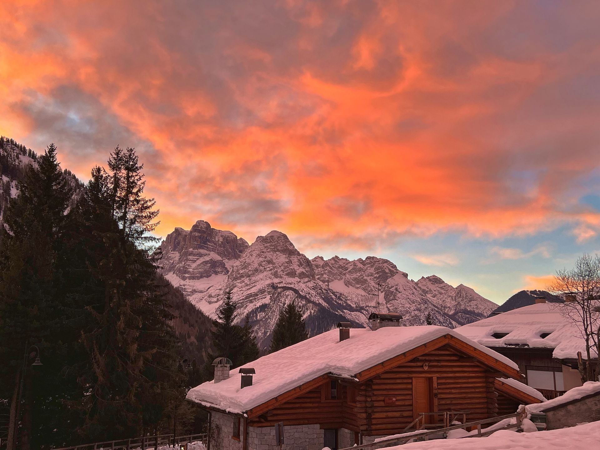 Una baita innevata in montagna con un tramonto sullo sfondo