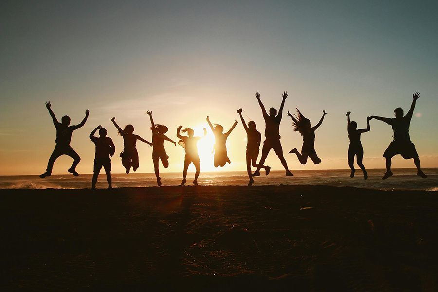 A group of people are jumping in the air on a beach at sunset.