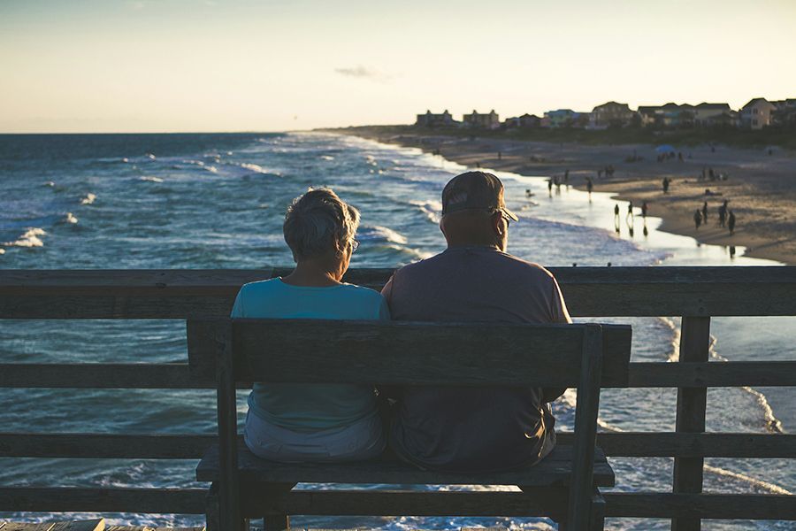 A man and a woman are sitting on a bench overlooking the ocean.