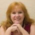 A woman with red hair is smiling with her hands folded.