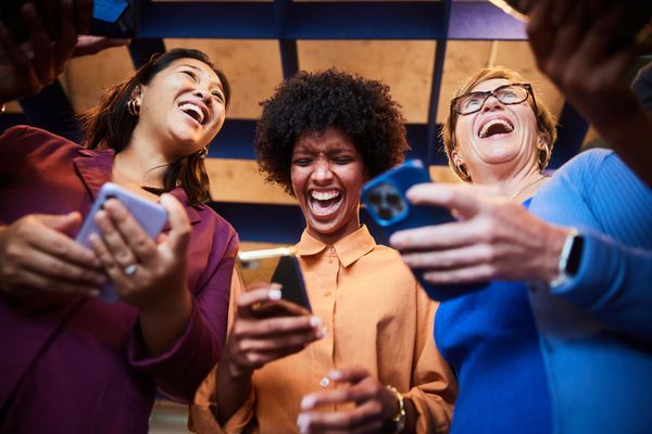 A group of women are laughing while looking at their phones.