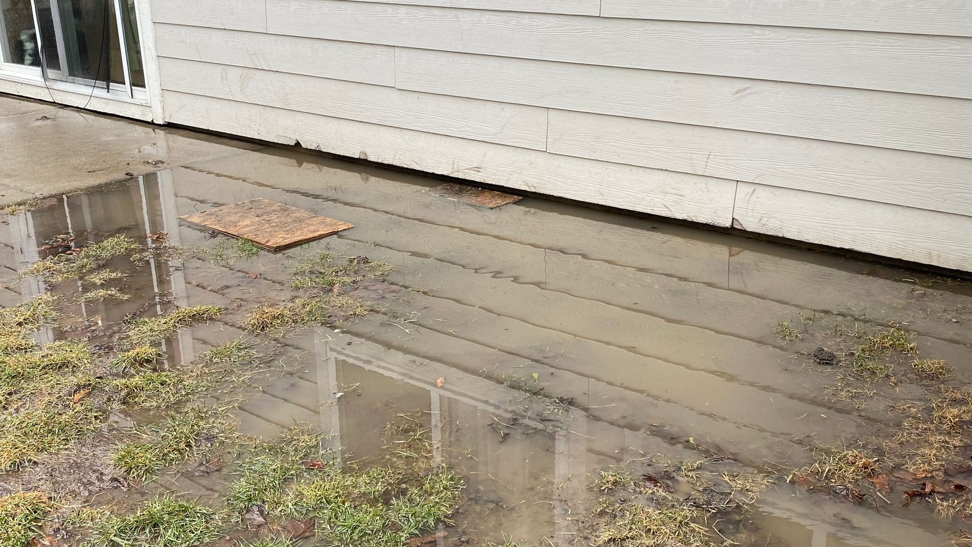 A flooded yard with a house in the background and a puddle of water on the ground.
