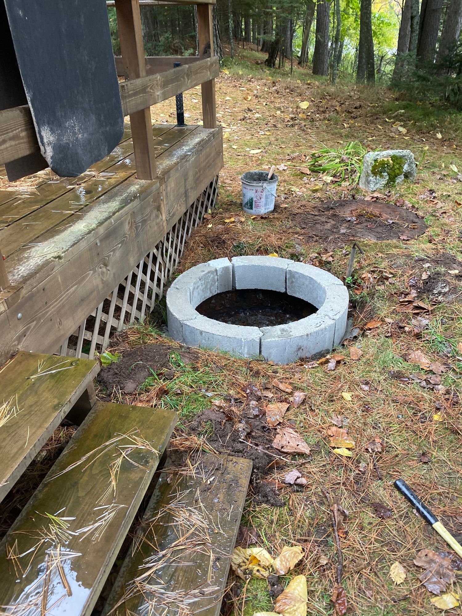A fire pit is being built next to a wooden deck.