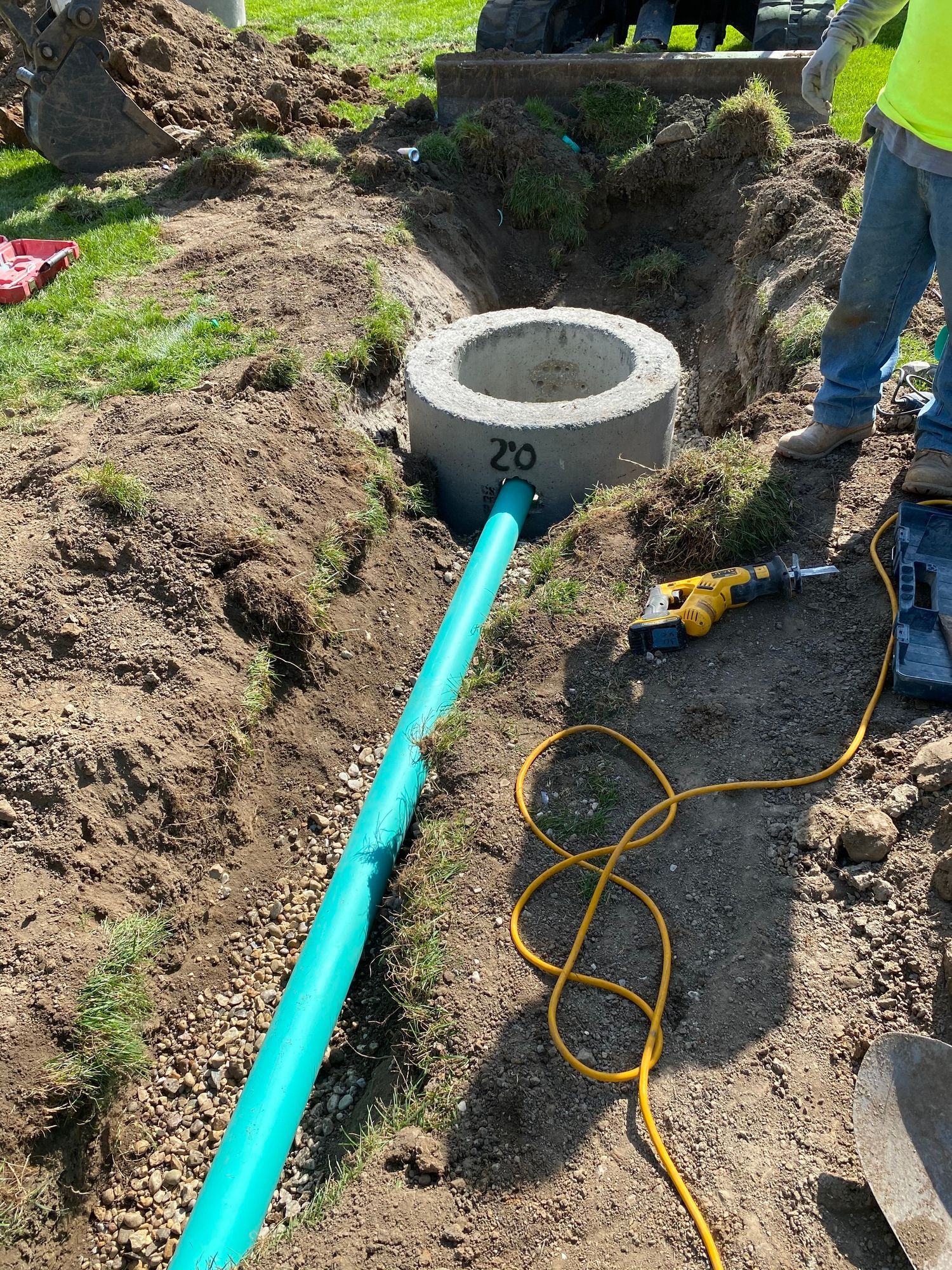 A man is standing next to a green pipe in the dirt.