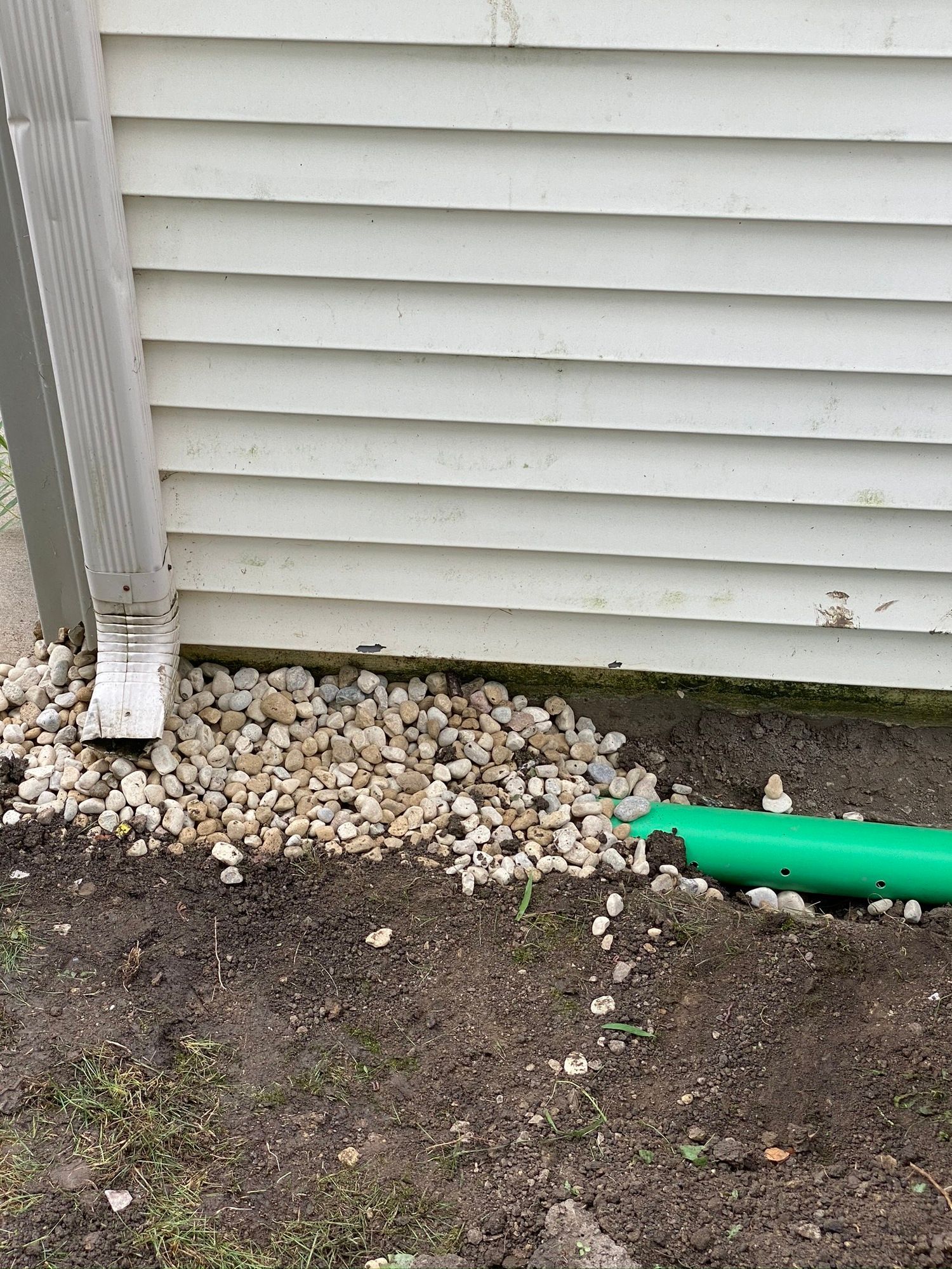 A green pipe is sitting in the dirt next to a white house.