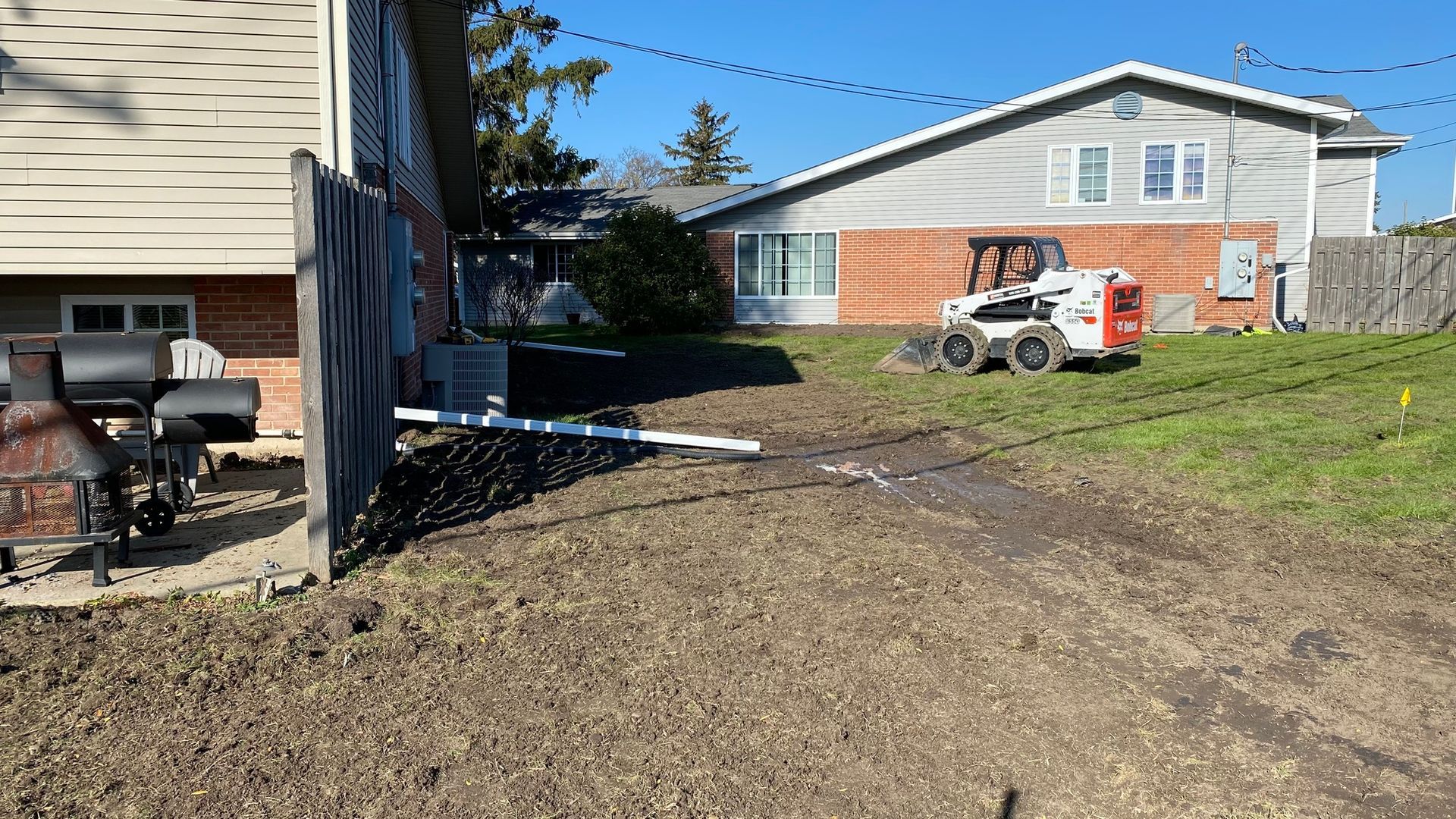A bobcat is driving down a dirt road in front of a house.