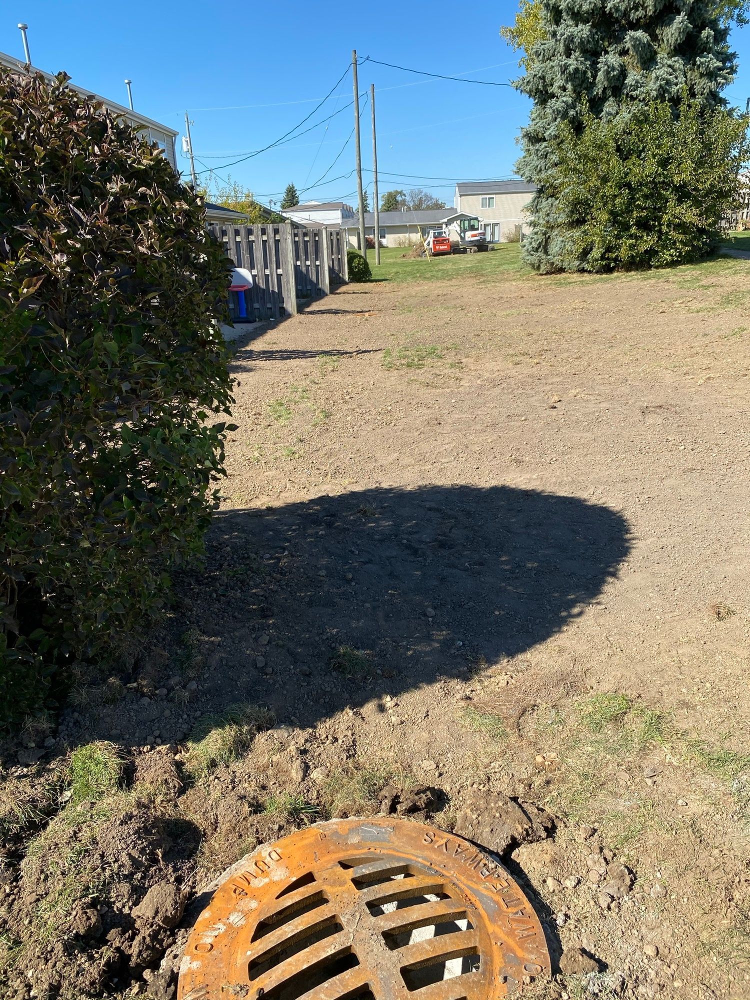 A rusty manhole cover is sitting in the middle of a dirt field.