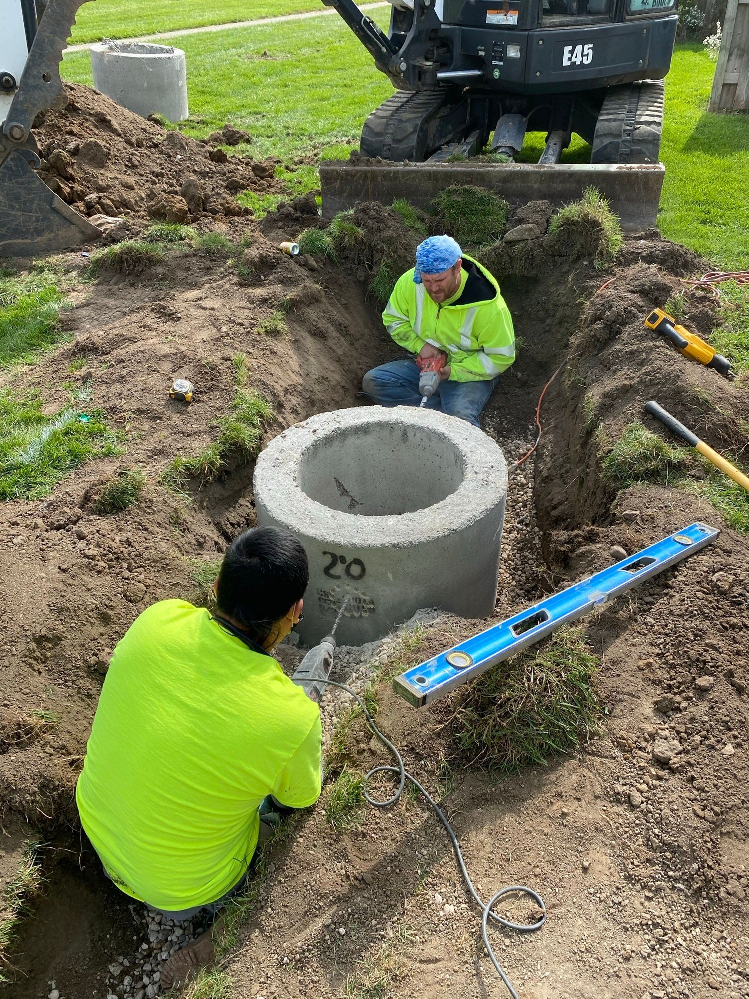 Two men are kneeling in the dirt next to a manhole cover.