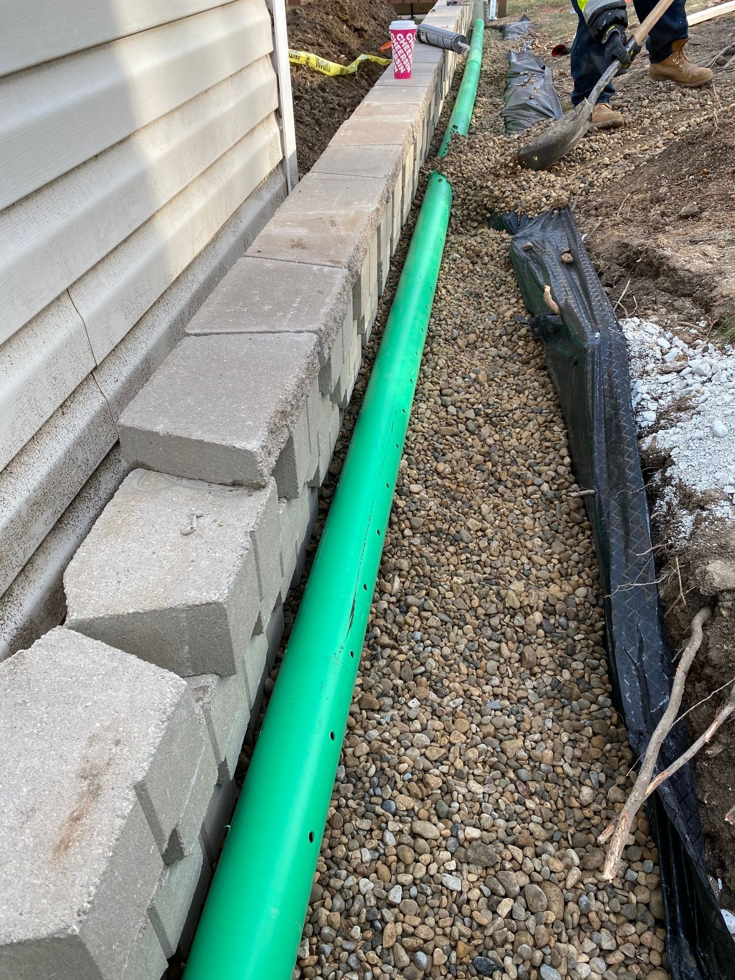 A green pipe is being installed next to a brick wall.