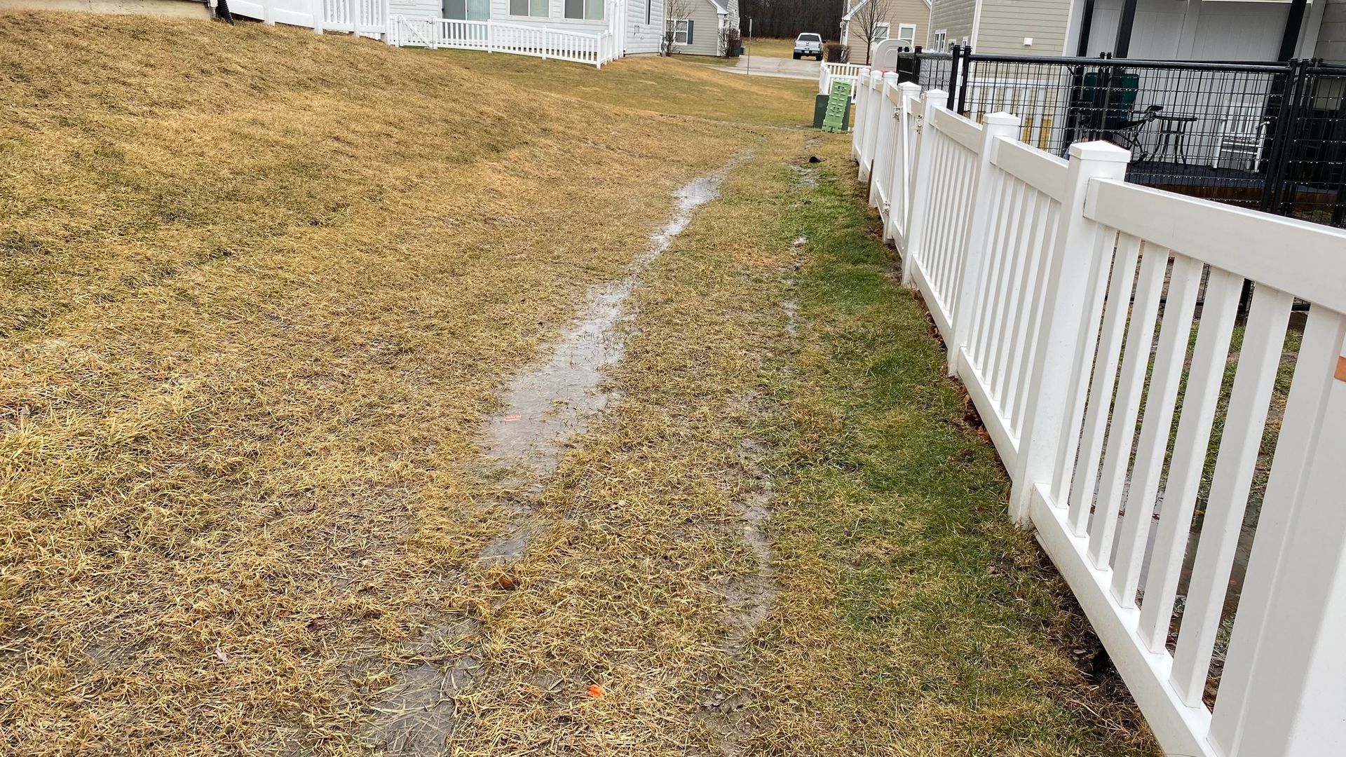 A white picket fence surrounds a muddy yard.