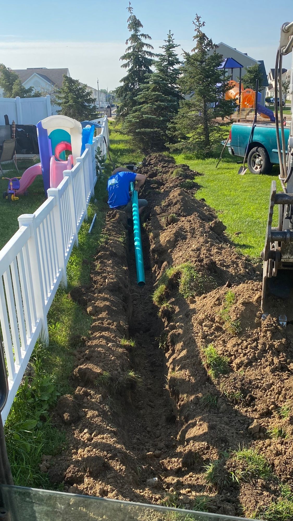 A hose is being installed in a yard next to a white fence.