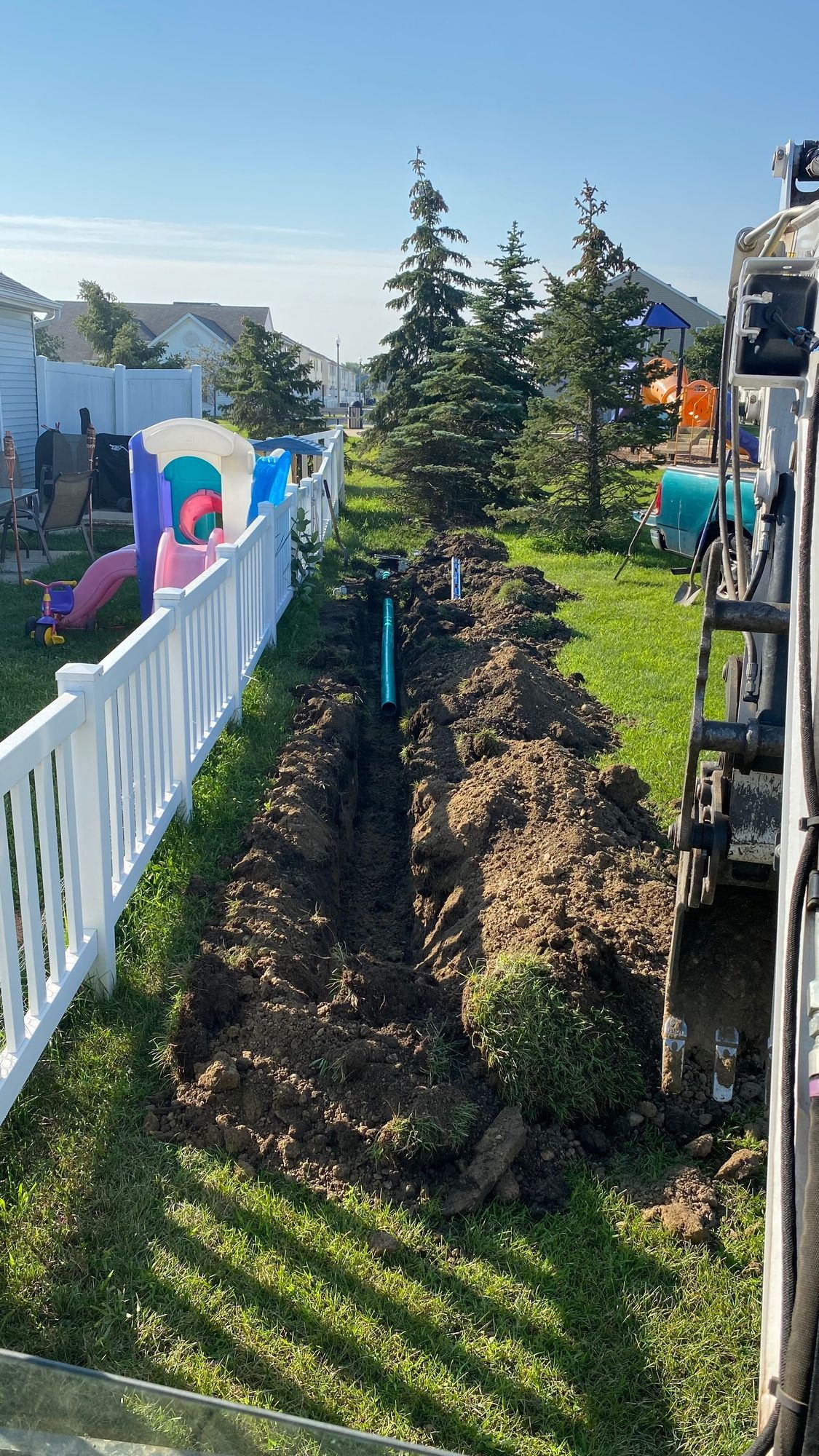 A large pile of dirt is being dug in a yard next to a white fence.