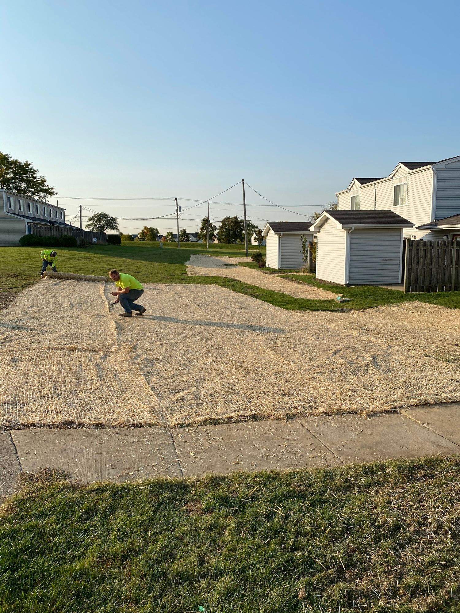 A man is kneeling down on a gravel driveway next to a sidewalk.